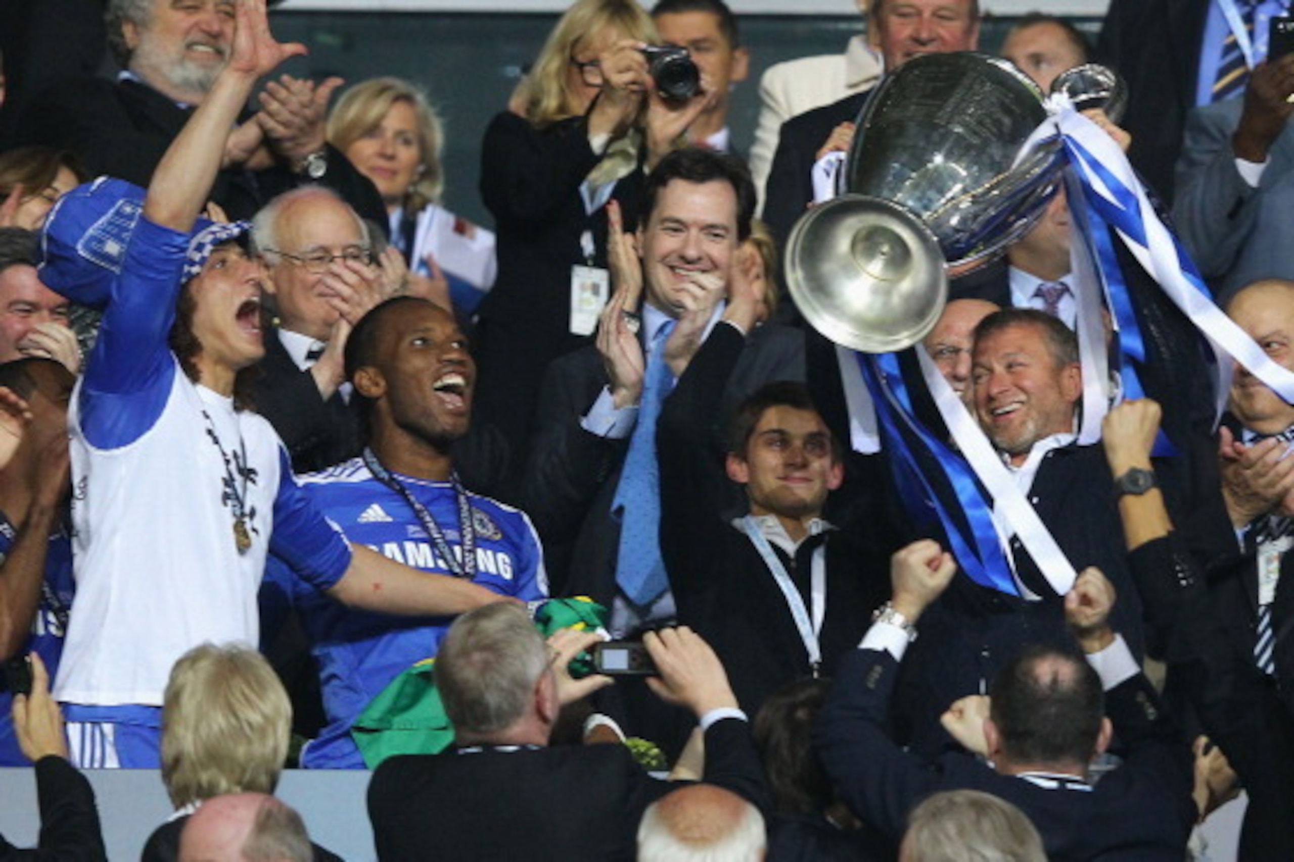 MUNICH, GERMANY - MAY 19:  Club owner Roman Abramovich (R) lifts the trophy in celebration while  Chancellor of the Exchequer George Osborne (C) applauds after their victory in the UEFA Champions League Final between FC Bayern Muenchen and Chelsea at the 