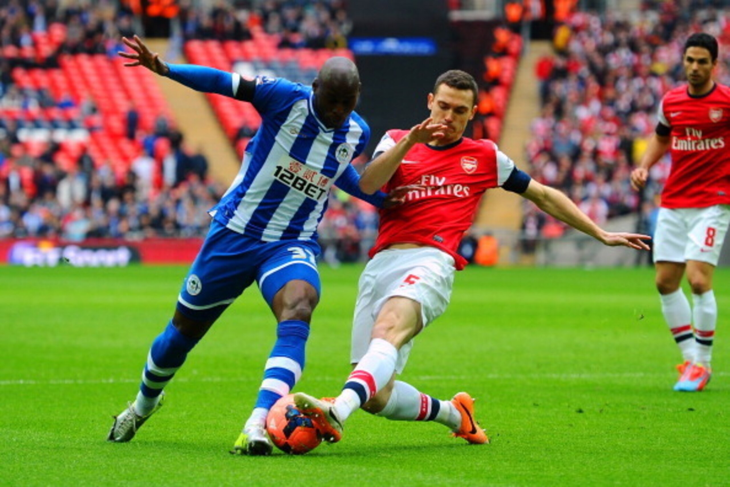 LONDON, ENGLAND - APRIL 12: Marc-Antoine Fortune of Wigan Athletic is tackled by Thomas Vermaelen of Arsenal during the FA Cup Semi-Final match between Wigan Athletic and Arsenal at Wembley Stadium on April 12, 2014 in London, England. (Photo by Mike He LONDON, ENGLAND - APRIL 12: Marc-Antoine Fortune of Wigan Athletic is tackled by Thomas Vermaelen of Arsenal during the FA Cup Semi-Final match between Wigan Athletic and Arsenal at Wembley Stadium on April 12, 2014 in London, England. (Photo by Mike He