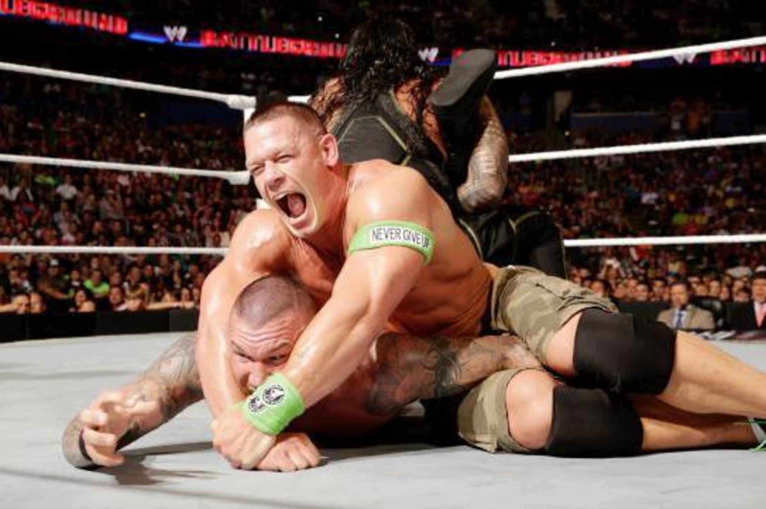 John Cena and Roman Reigns both apply a submission hold to Randy Orton.