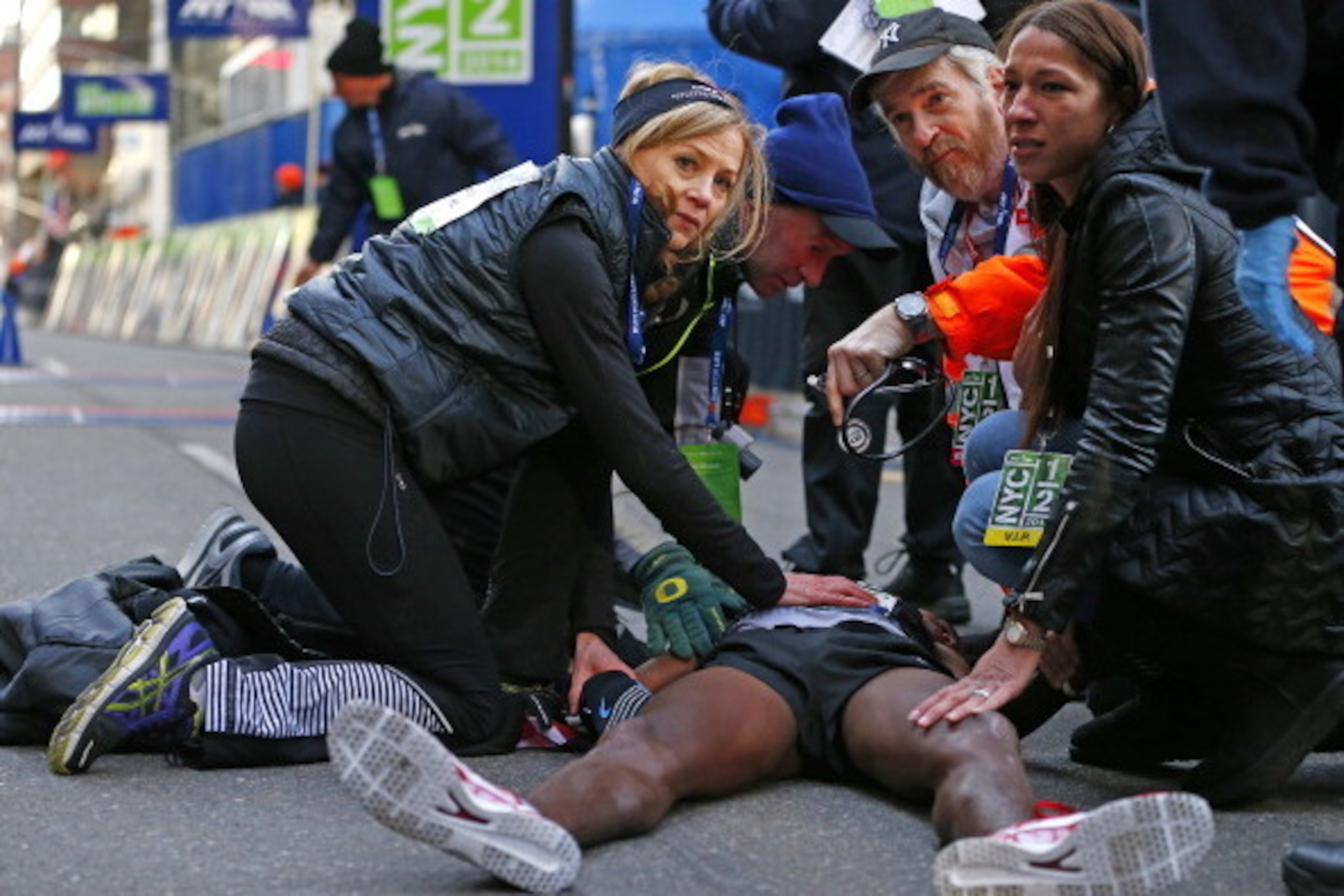 NEW YORK, NY - MARCH 16: Mo Farah of Great Britain is taken care of by medical personal and Mary Wittenberg, the President of the New York Road Runners Club (L) after he collapsed at the finish line after finishing in second place at the 2014 New York Cit