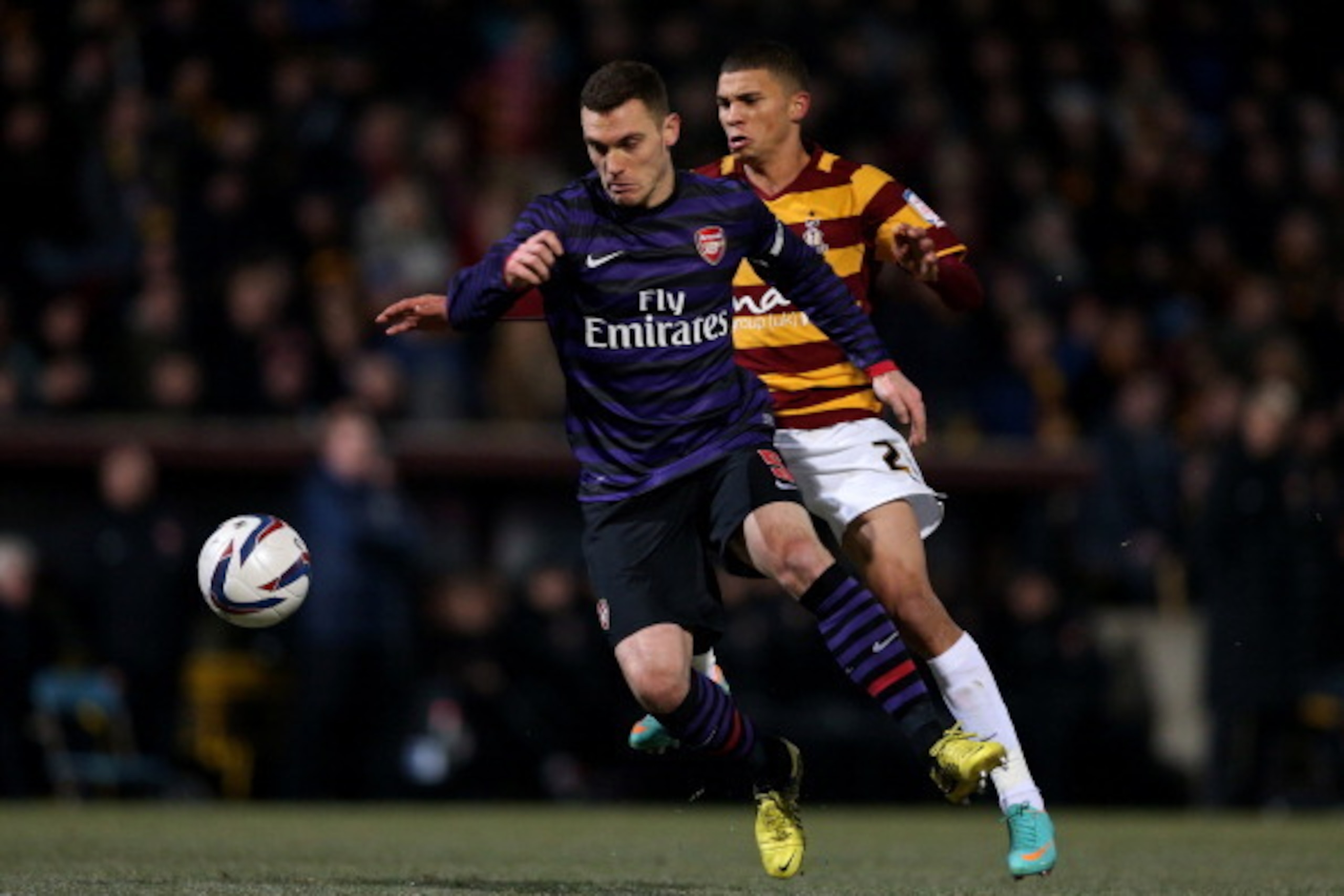 BRADFORD, ENGLAND - DECEMBER 11:  Thomas Vermaelen of Arsenal controls the ball as Nahki Wells of Bradford closes min during the Capital One Cup quarter final match between Bradford City and Arsenal at the Coral Windows Stadium, Valley Parade on December 