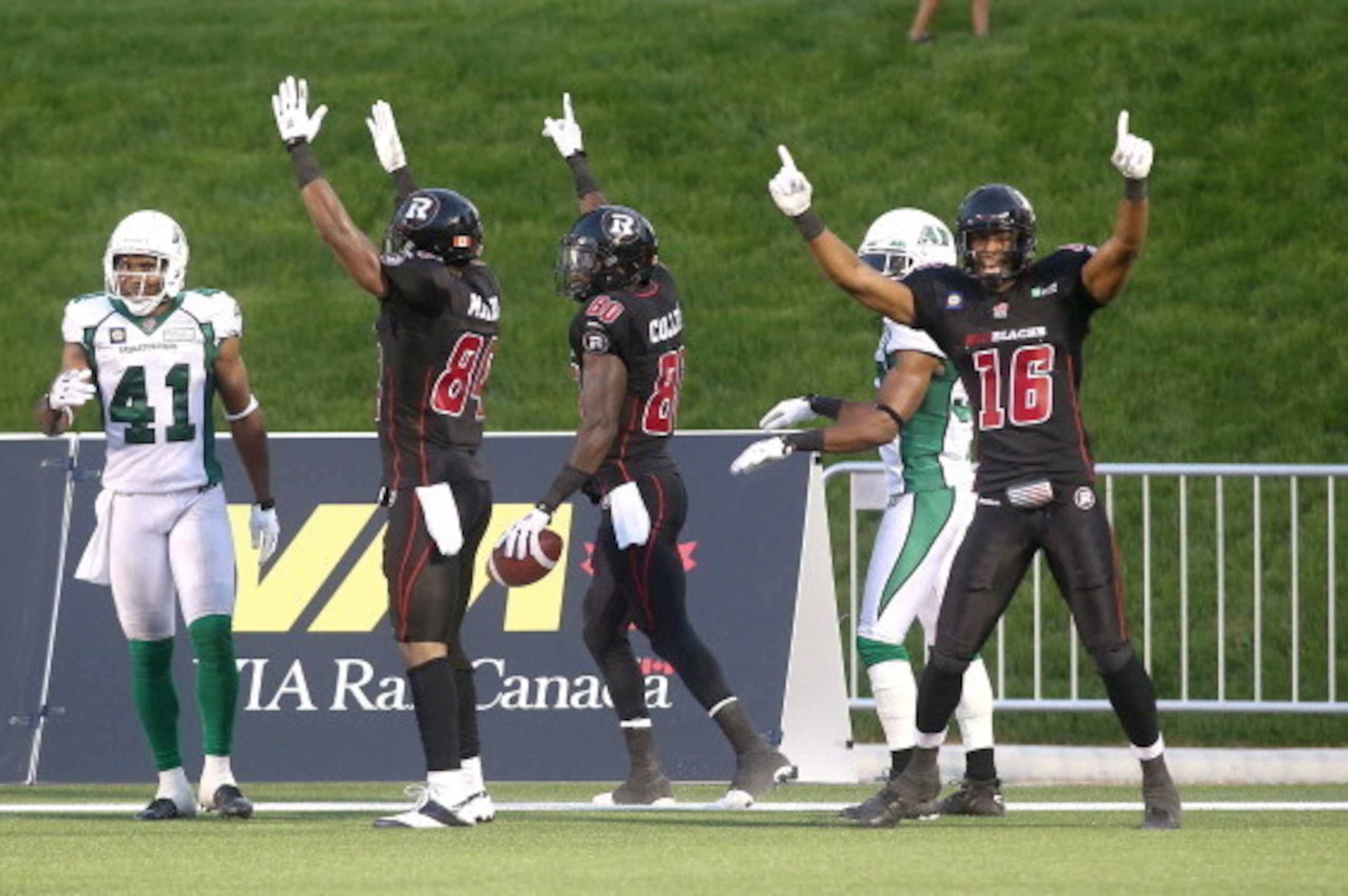OTTAWA, ON, CANADA - AUGUST 2: Dobson Collins #80 of the Ottawa Redblacks celebrates a touchdown with teammates Wallace Miles #84 and Marcus Henry #16 as Tyron Brackenridge #41 of the Saskatchewan Roughriders looks on during a CFL game at TD Place Stadium