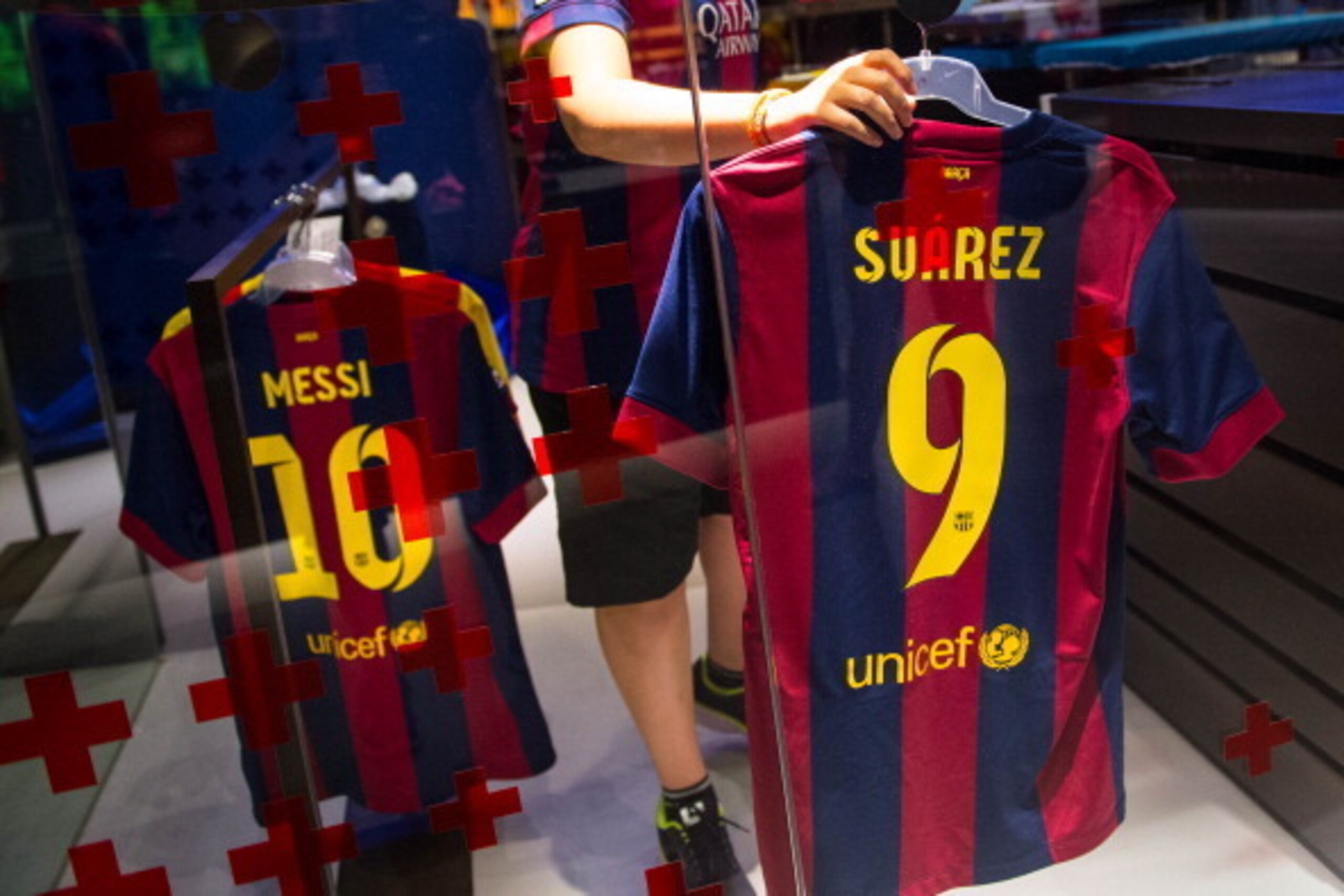BARCELONA, SPAIN - JULY 12:  An employee hangs a Luis Suarez shirt next to a Leo Messi shirt after printing his name and number on it at the FC Barcelona official store on July 12, 2014 in Barcelona, Spain.  (Photo by David Ramos/Getty Images)