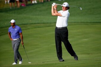 LOUISVILLE, KY - AUGUST 07:  Phil Mickelson (R) of the United States hits an approach shot on the tenth hole as Tiger Woods (L) of the United States looks on during the first round of the 96th PGA Championship at Valhalla Golf Club on August 7, 2014 in Lo