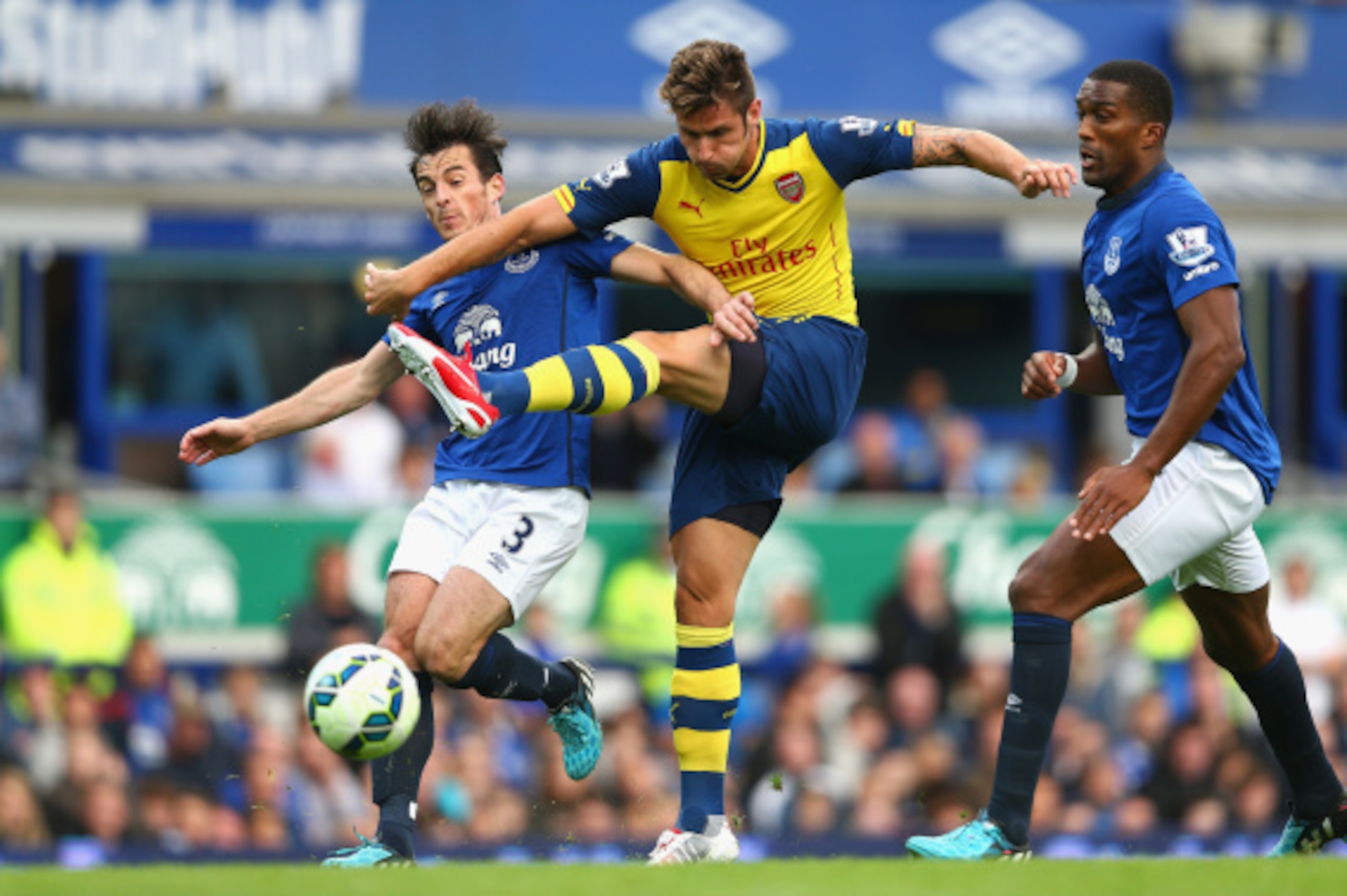 LIVERPOOL, ENGLAND - AUGUST 23:  Olivier Giroud of Arsenal shoots at goal under pressure from Leighton Baines  and Sylvain Distin of Everton during the Barclays Premier League match between Everton and Arsenal at Goodison Park on August 23, 2014 in Liverp