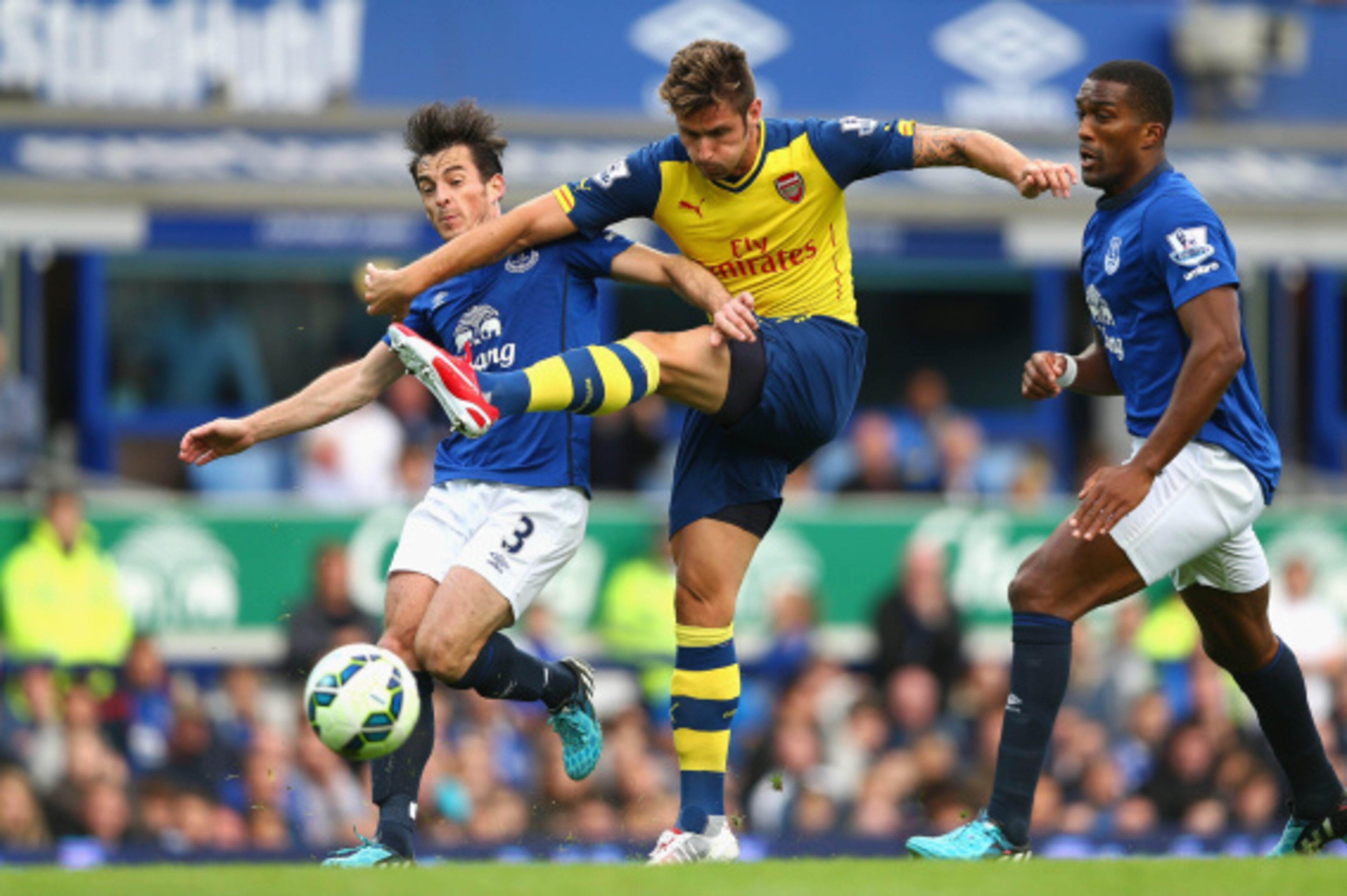 LIVERPOOL, ENGLAND - AUGUST 23:  Olivier Giroud of Arsenal shoots at goal under pressure from Leighton Baines  and Sylvain Distin of Everton during the Barclays Premier League match between Everton and Arsenal at Goodison Park on August 23, 2014 in Liverp