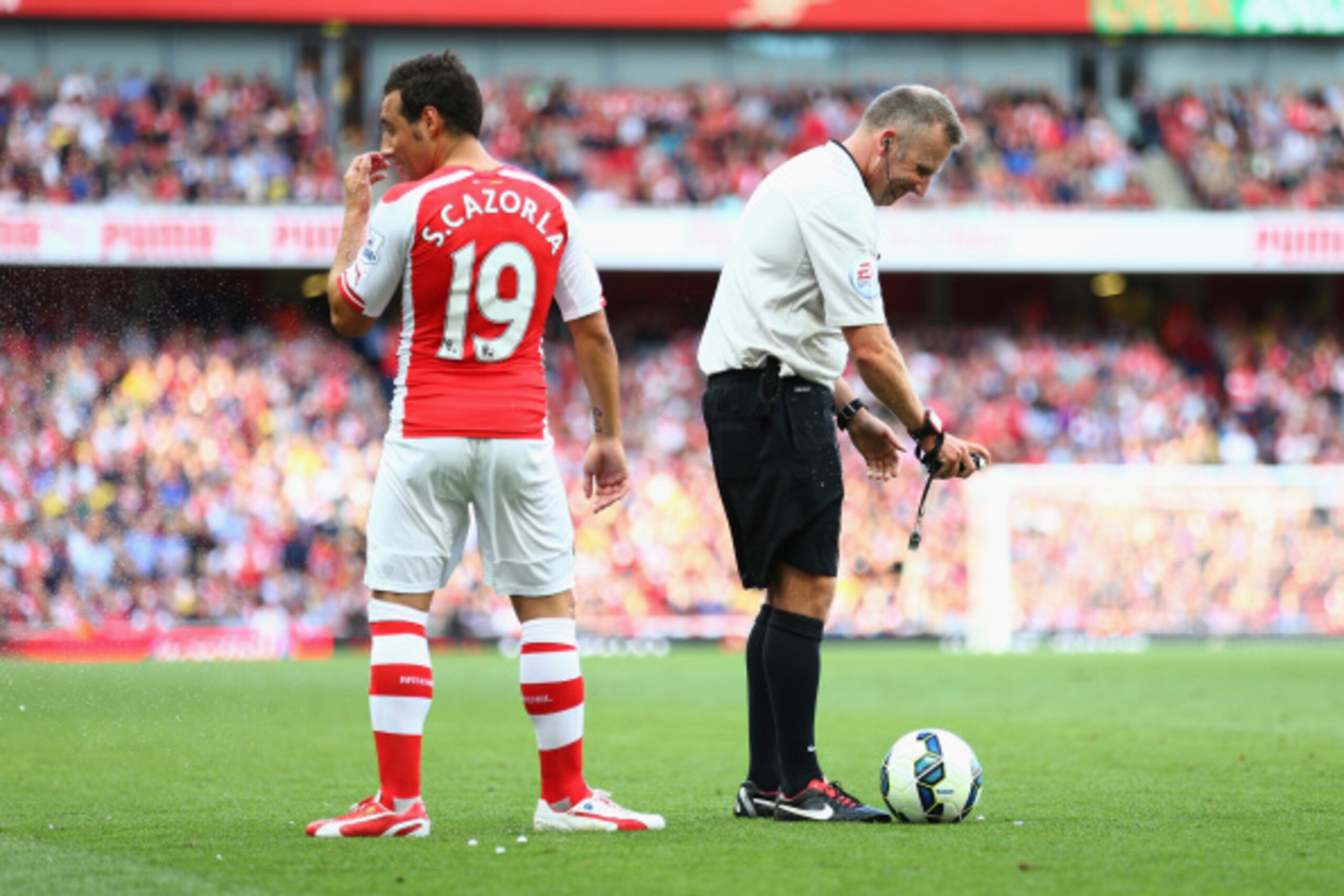 LONDON, ENGLAND - AUGUST 16:  Referee Jon Moss struggles with the vanishing spray and Santi Cazorla of Arsenal gets a face full during the Barclays Premier League match between Arsenal and Crystal Palace at Emirates Stadium on August 16, 2014 in London, E