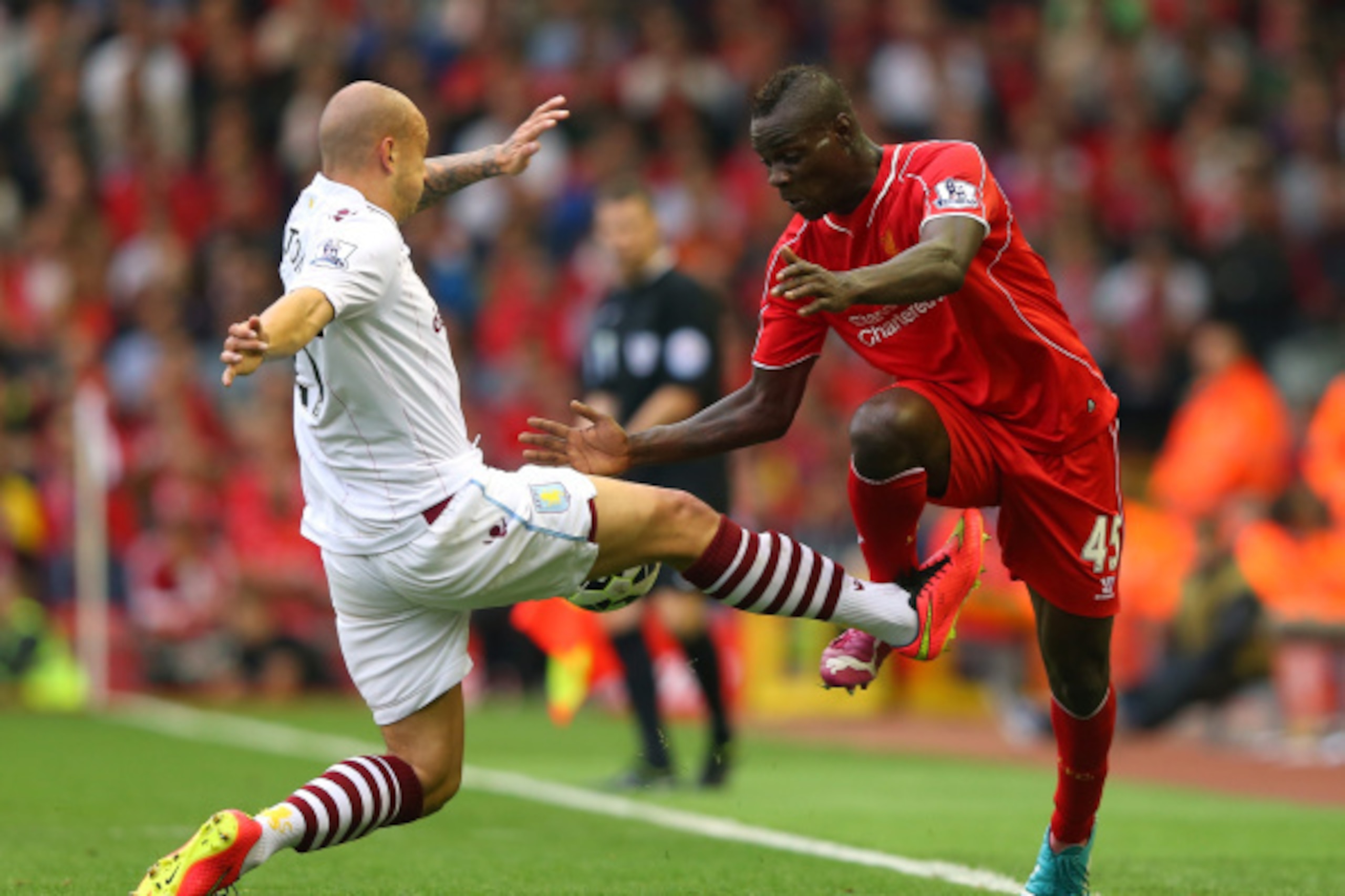 LIVERPOOL, ENGLAND - SEPTEMBER 13:  Mario Balotelli of Liverpool is tackled from Alan Hutton of Aston Villa during the Barclays Premier League match between Liverpool and Aston Villa at Anfield on September 13, 2014 in Liverpool, England.  (Photo by Alex 