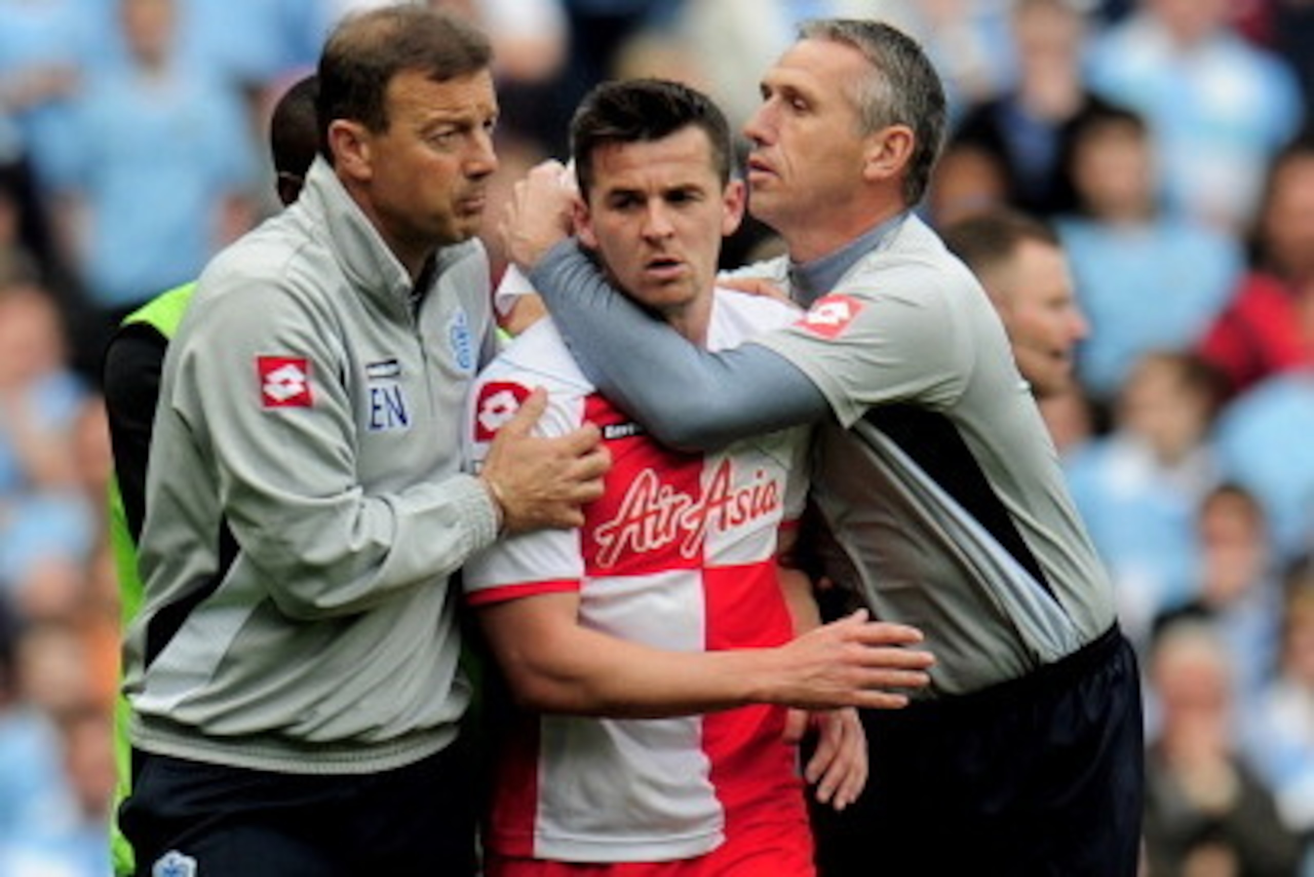 MANCHESTER, ENGLAND - MAY 13:  Joey Barton of QPR is restrained by QPR First Team Coach Eddie Niedzwiecki (L) and QPR Goalkeeping Coach Kevin Hitchcock (R) after being shown the red card by Referee Mike Dean during the Barclays Premier League match betwee