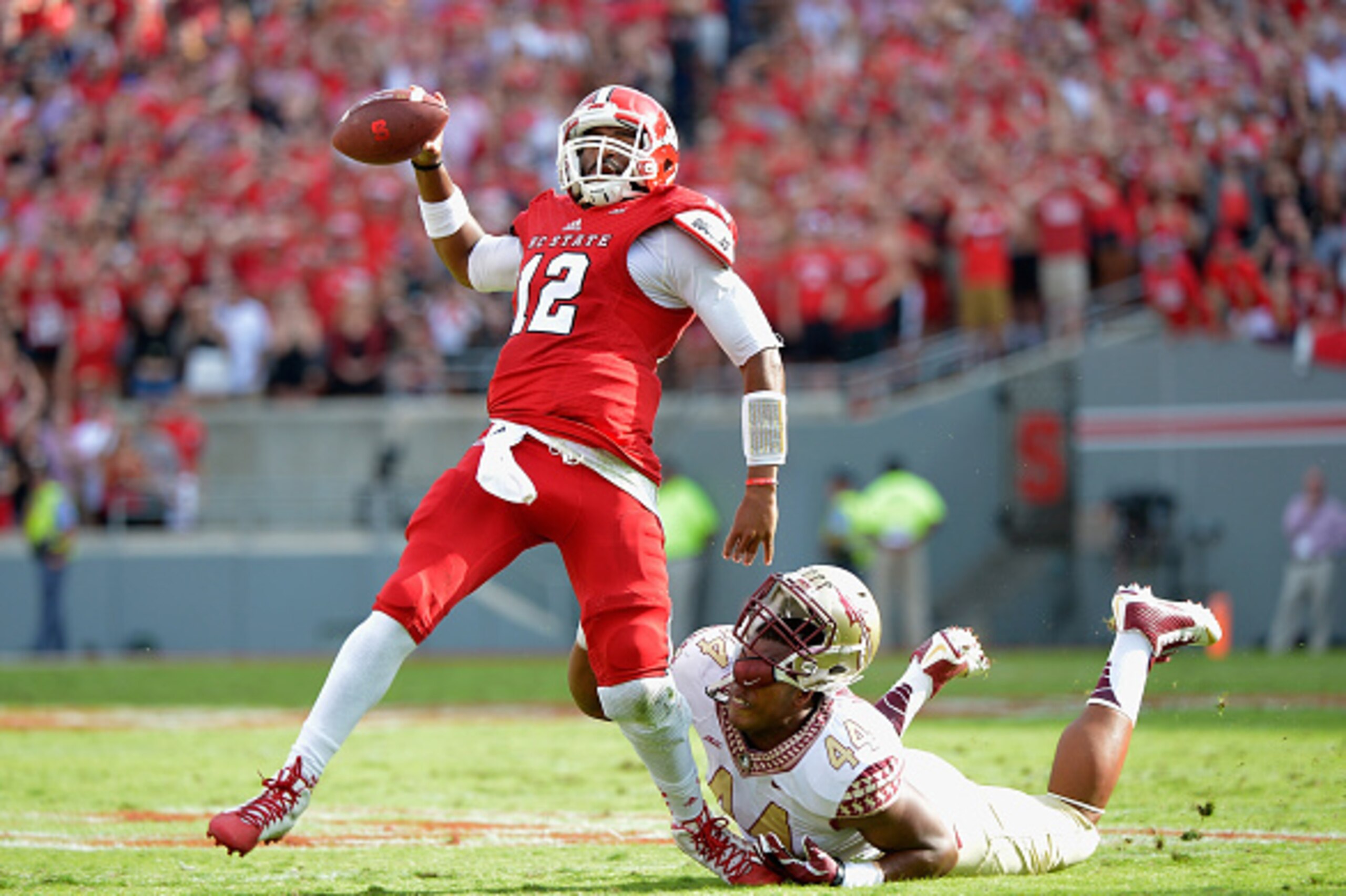 RALEIGH, NC - SEPTEMBER 27: Jacoby Brissett #12 of the North Carolina State Wolfpack breaks free from DeMarcus Walker #44 of the Florida State Seminoles to throw a touchdown pass during the first quarter of their game at Carter-Finley Stadium on September