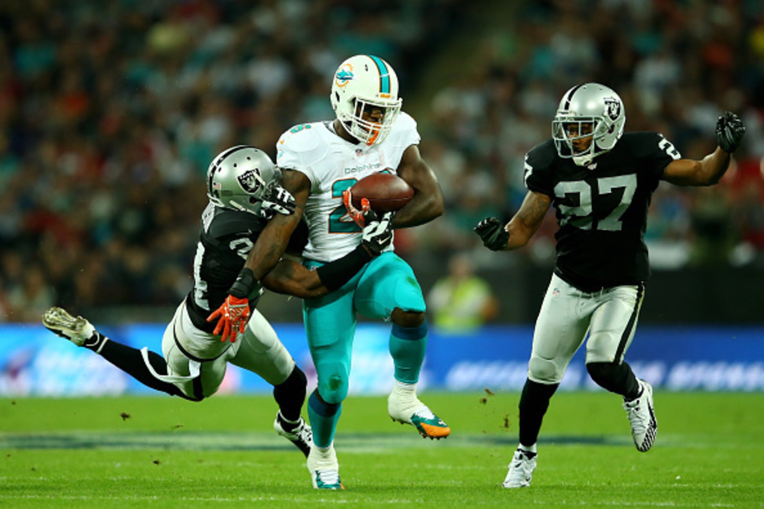 LONDON, ENGLAND - SEPTEMBER 28:  Lamar Miller #26 of the Miami Dolphins is tackled by Charles Woodson #24 of the Oakland Raiders and Carlos Rogers #27 of the Oakland Raiders during the NFL match between the Oakland Raiders and the Miami Dolphins at Wemble