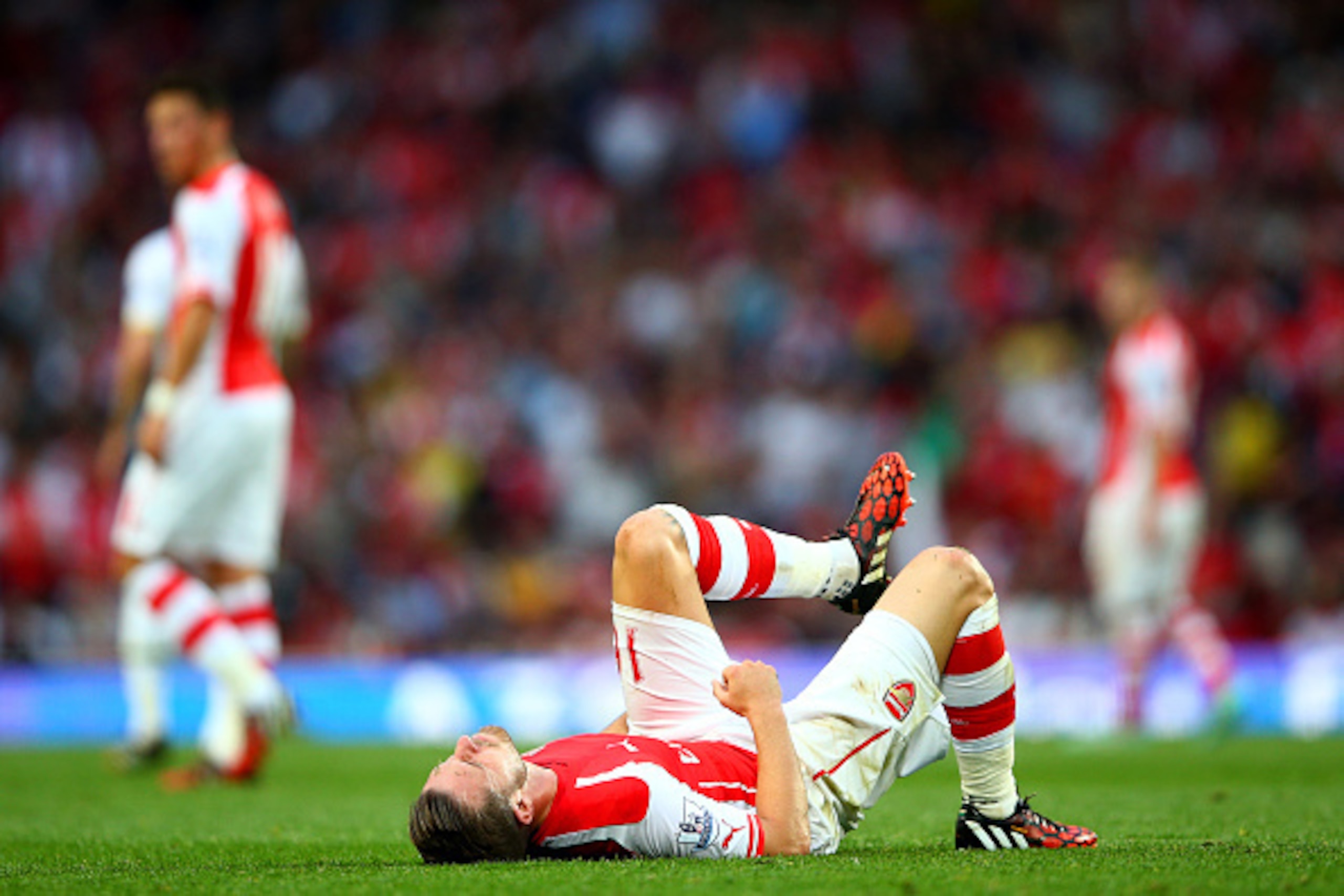 LONDON, ENGLAND - SEPTEMBER 27:  Aaron Ramsey of Arsenal holds his leg as he lies on the pitch after picking up an injury during the Barclays Premier League match between Arsenal and Tottenham Hotspur at Emirates Stadium on September 27, 2014 in London, E