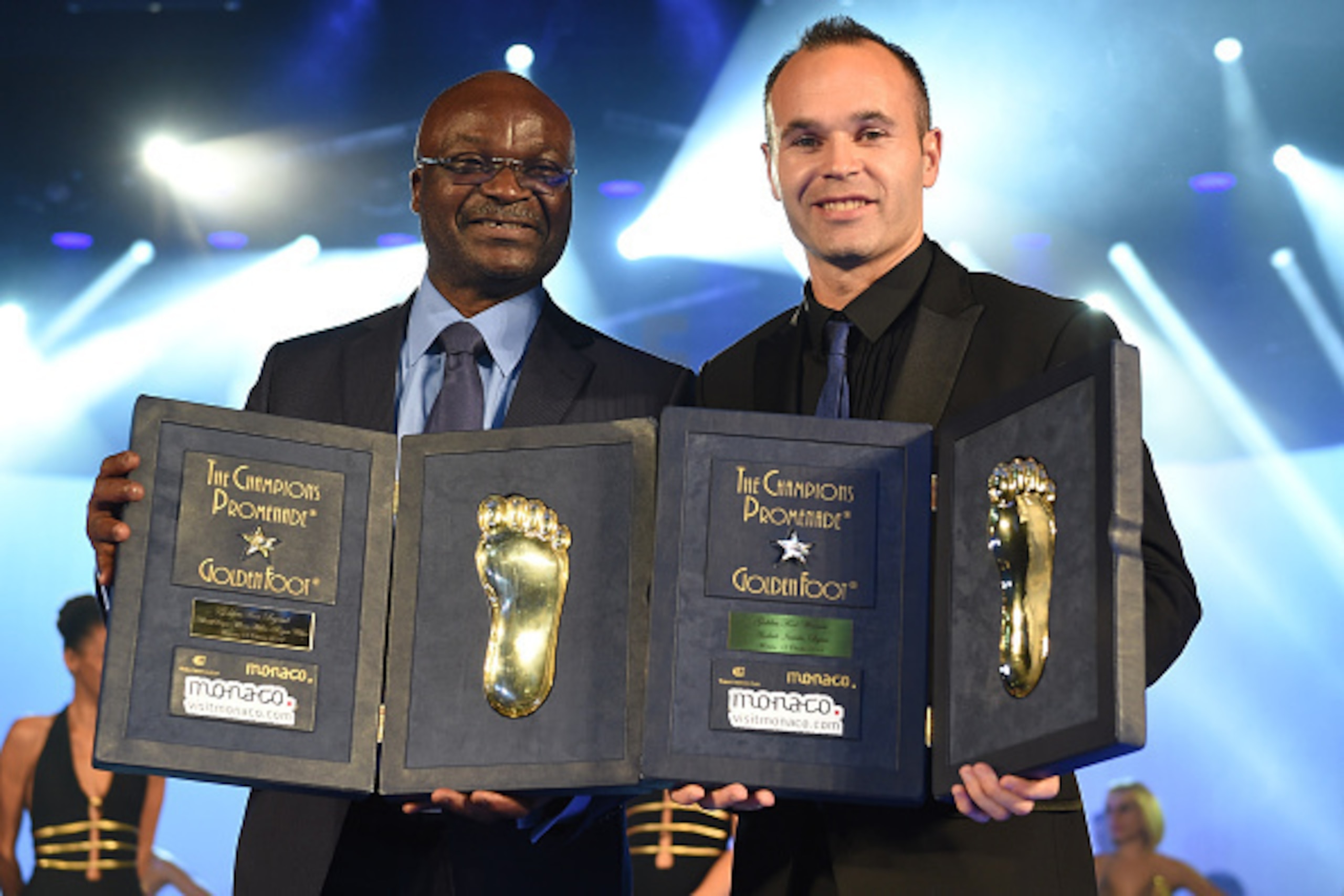 MONTE-CARLO, MONACO - OCTOBER 13:  Roger Milla (L) and Andres Iniesta receive the Golden Foot Award trophy during the Golden Foot Award 2014 ceremony at Sporting Club on October 13, 2014 in Monte-Carlo, Monaco.  (Photo by Valerio Pennicino/Getty Images fo