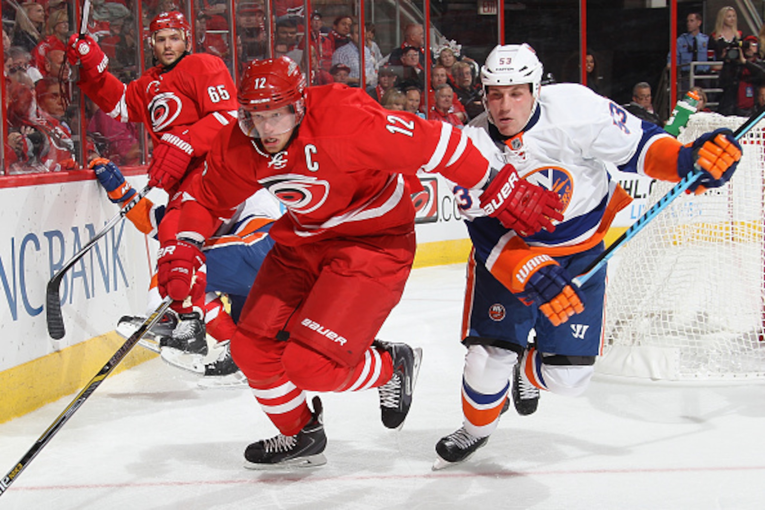 RALEIGH, NC - OCTOBER 10: Eric Staal #12 of the Carolina Hurricanes and Casey Cizikas #53 of the New York Islanders skate hard into the corner for the puck during their NHL game at PNC Arena on October 10, 2014 in Raleigh, North Carolina.  (Photo by Gregg