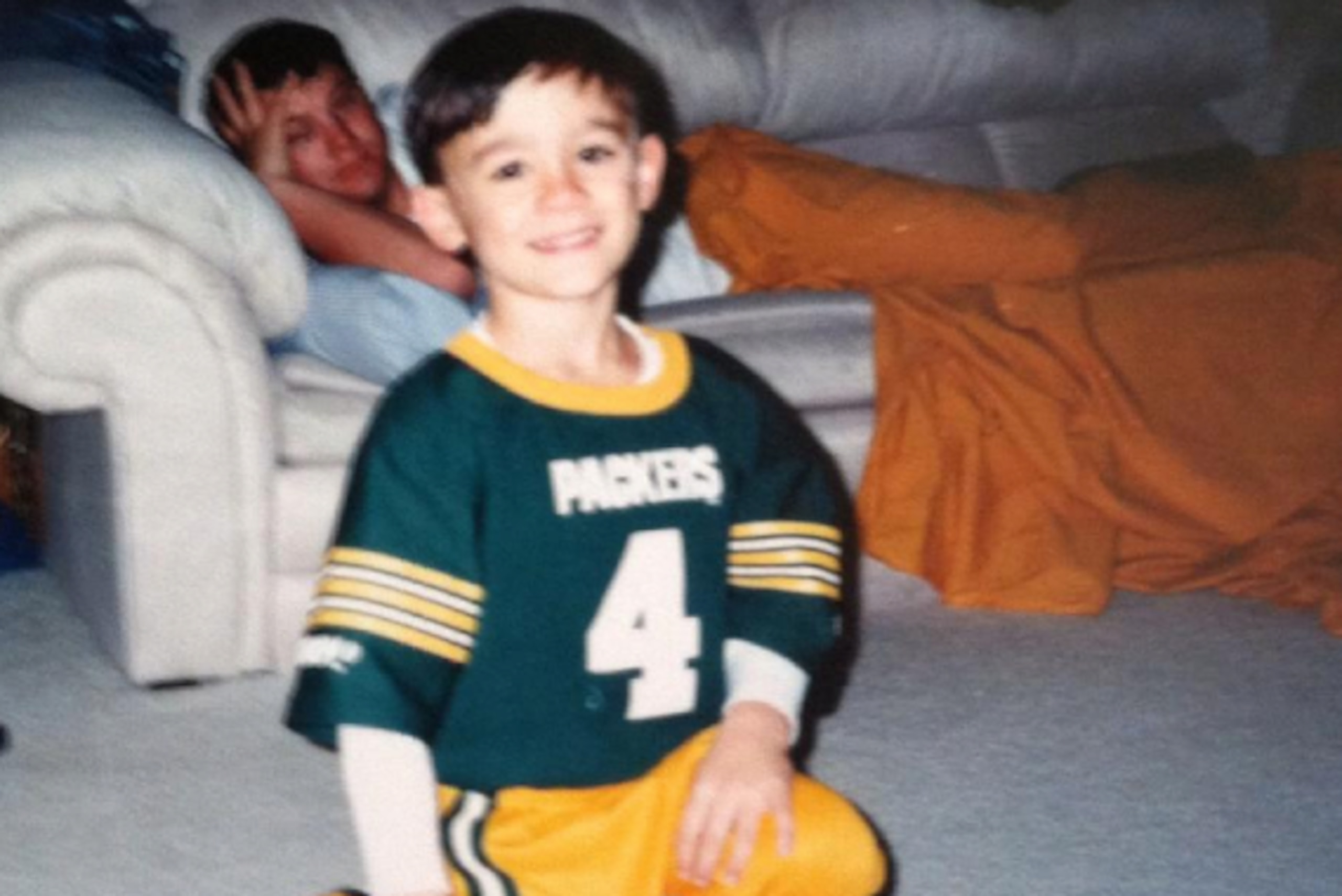 Dylan Favre in Uncle Brett's Packers jersey as his father Jeff rests on the couch.