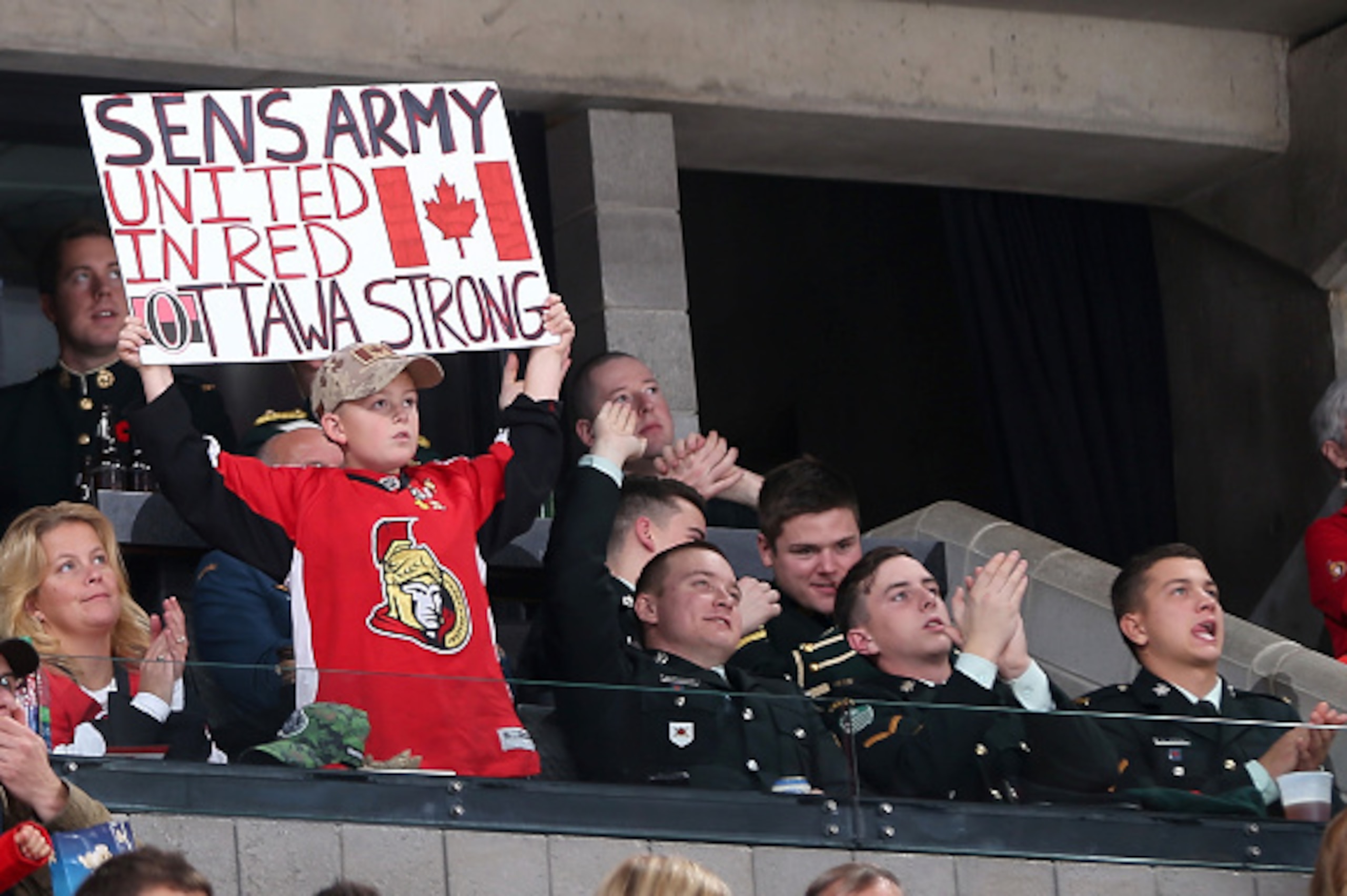 OTTAWA, ON - OCTOBER 25: A young fan surrounded by military personnel holds an 'Ottawa Strong' sign during an NHL game between the Ottawa Senators and the New Jersey Devils at Canadian Tire Centre on October 25, 2014 in Ottawa, Ontario, Canada. (Photo by OTTAWA, ON - OCTOBER 25: A young fan surrounded by military personnel holds an 'Ottawa Strong' sign during an NHL game between the Ottawa Senators and the New Jersey Devils at Canadian Tire Centre on October 25, 2014 in Ottawa, Ontario, Canada. (Photo by
