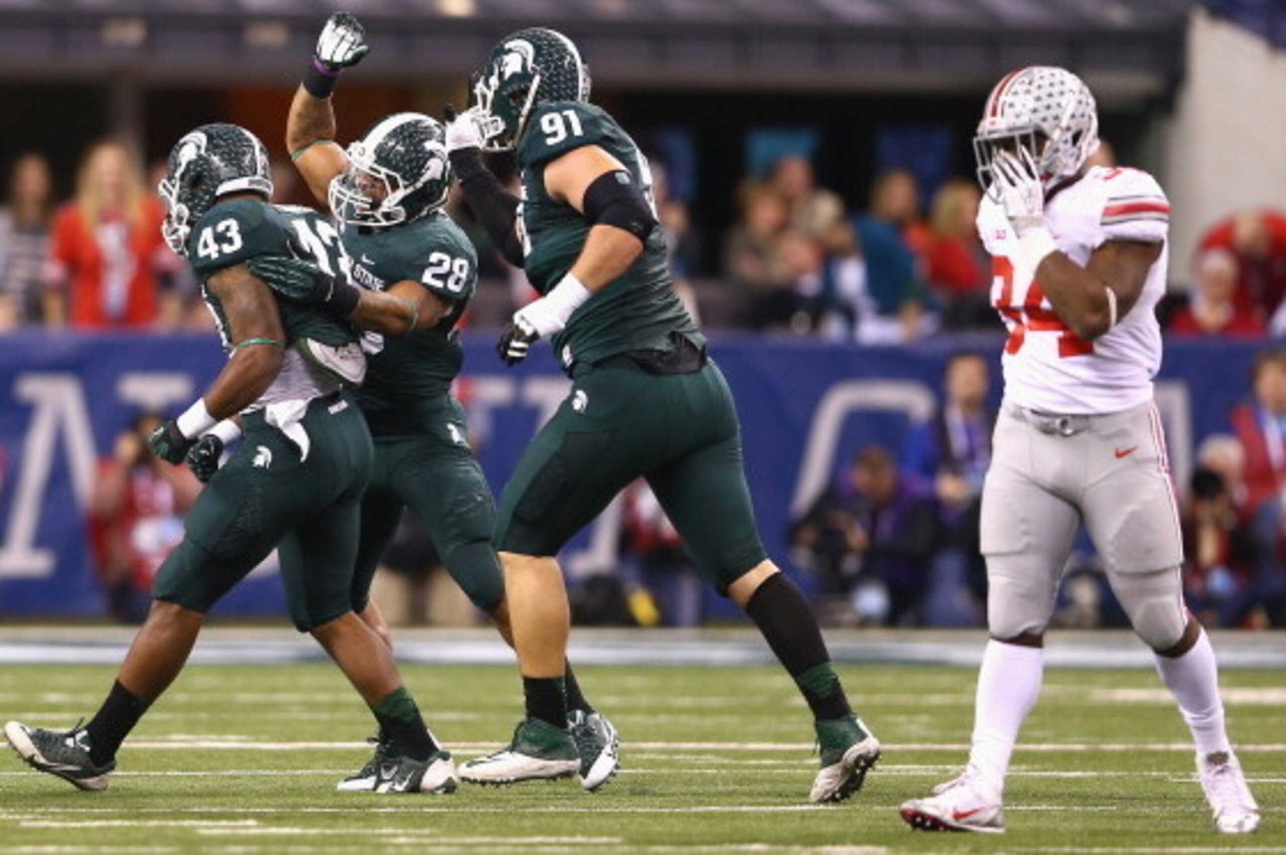INDIANAPOLIS, IN - DECEMBER 07:  Ed Davis #43, Denicos Allen #28 and Tyler Hoover #91  of the Michigan State Spartans celebrate a sack as Jamal Marcus #34 of the Ohio State Buckeyes walks away during the Big Ten Conference Championship game at Lucas Oil S