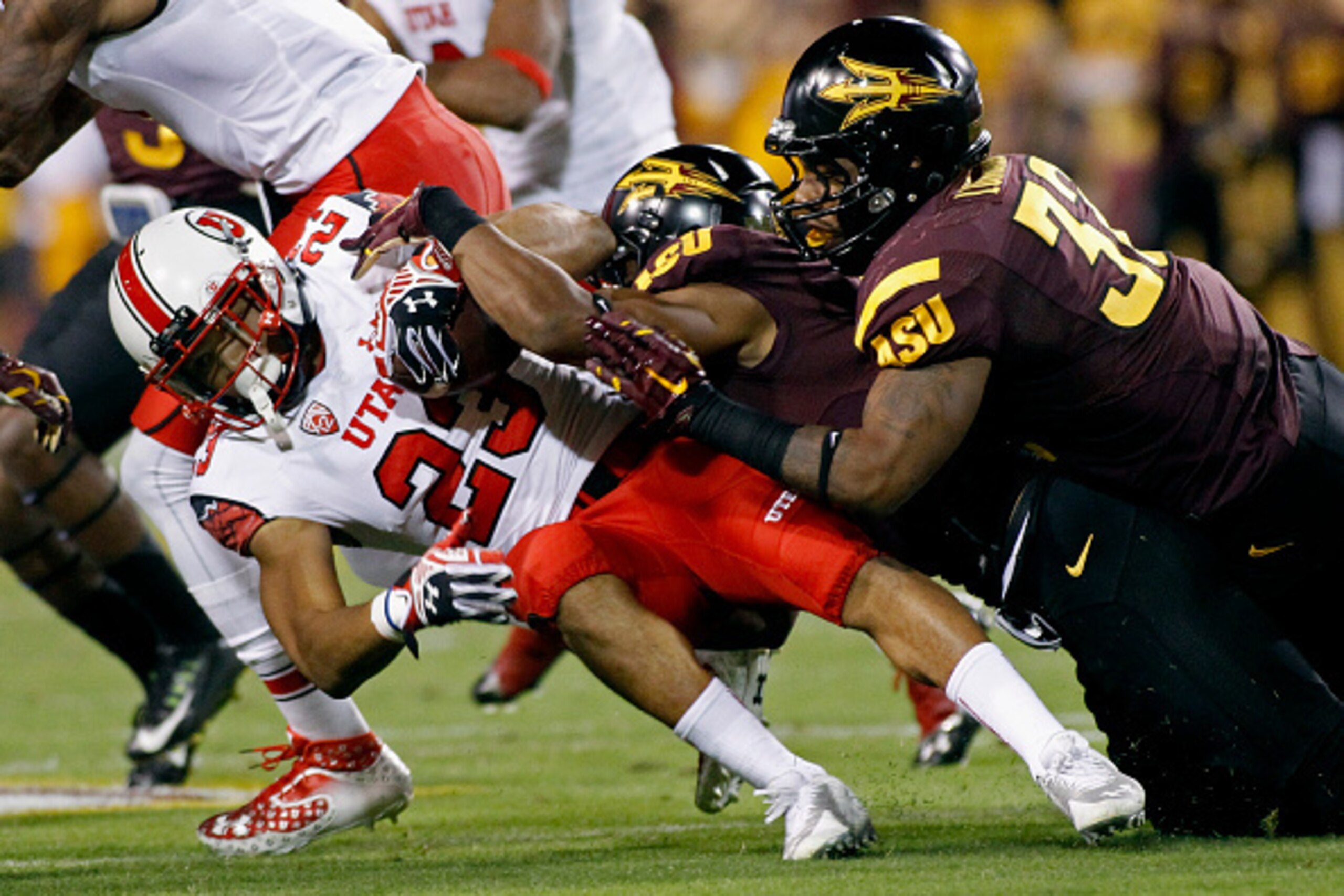 TEMPE, AZ - NOVEMBER 01:  Running back Devontae Booker #23 of the Utah Utes lunges forward for yardage as he is tackled by a pair of Arizona State Sun Devils defenders during the first quarter of a college football game at Sun Devil Stadium on November 1,