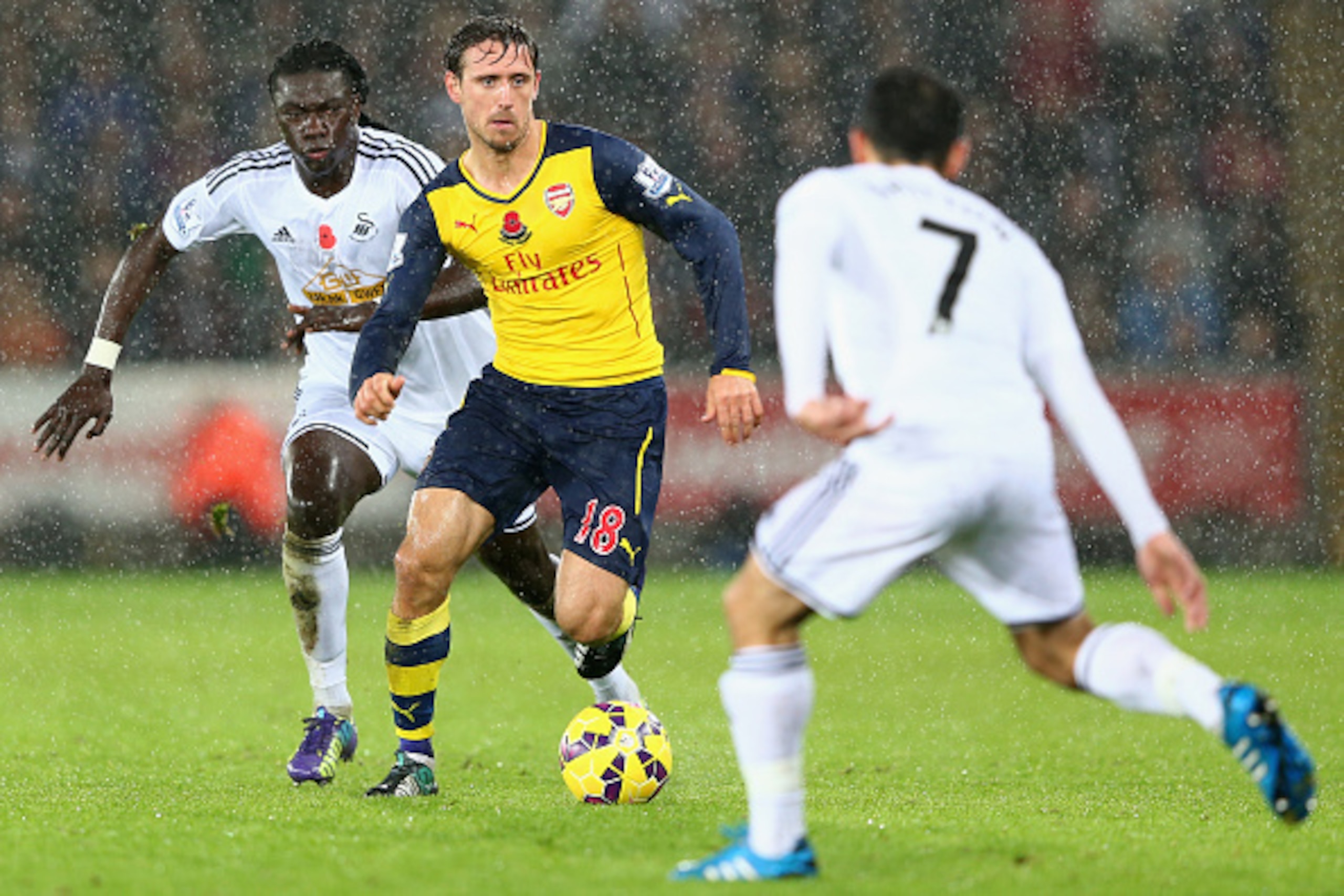 SWANSEA, WALES - NOVEMBER 09:  Nacho Monreal (C) of Arsenal is tracked by Bafetimbi Gomis (L) and Leon Britton (R) of Swansea during the Barclays Premier League match between Swansea City and Arsenal at the Liberty Stadium on November 9, 2014 in Swansea, 