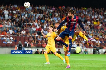 BARCELONA, SPAIN - SEPTEMBER 17:  Gerard Pique of FC Barcelona heads the ball towards goal under a challenge by Joao Guilherme of APOEL FC during the UEFA Champions League Group F match between FC Barcelona and APOEL FC at the Camp Nou Stadium on Septembe