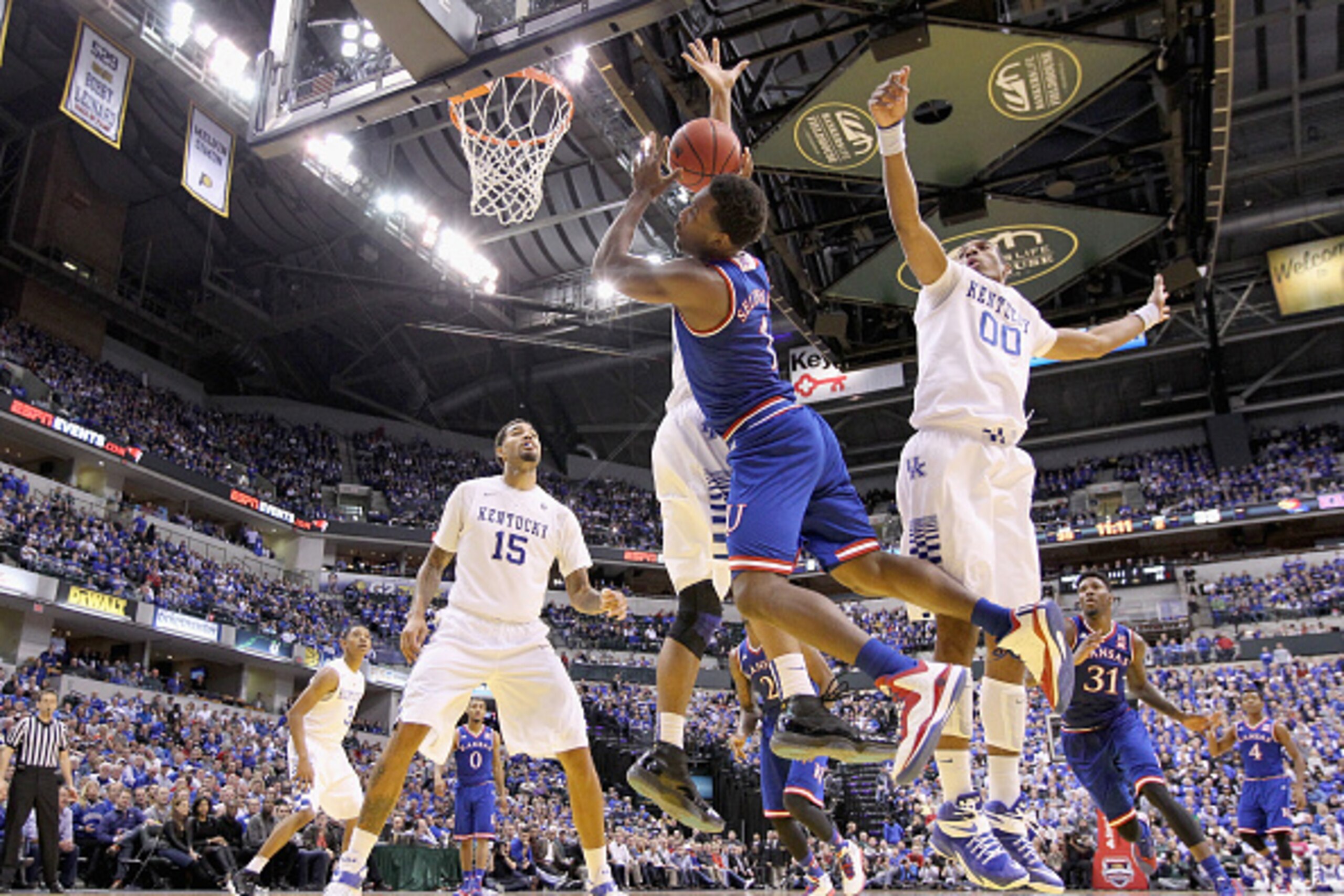 INDIANAPOLIS, IN - NOVEMBER 18: Wayne Seldon #1 of the Kansas Jayhawks loses control of the ball  while defended by Trey Lyles #41 and Marcus Lee #00 of the Kentucky Wildcats in the State Farm Champions Classic at Bankers Life Fieldhouse on November 18, 2