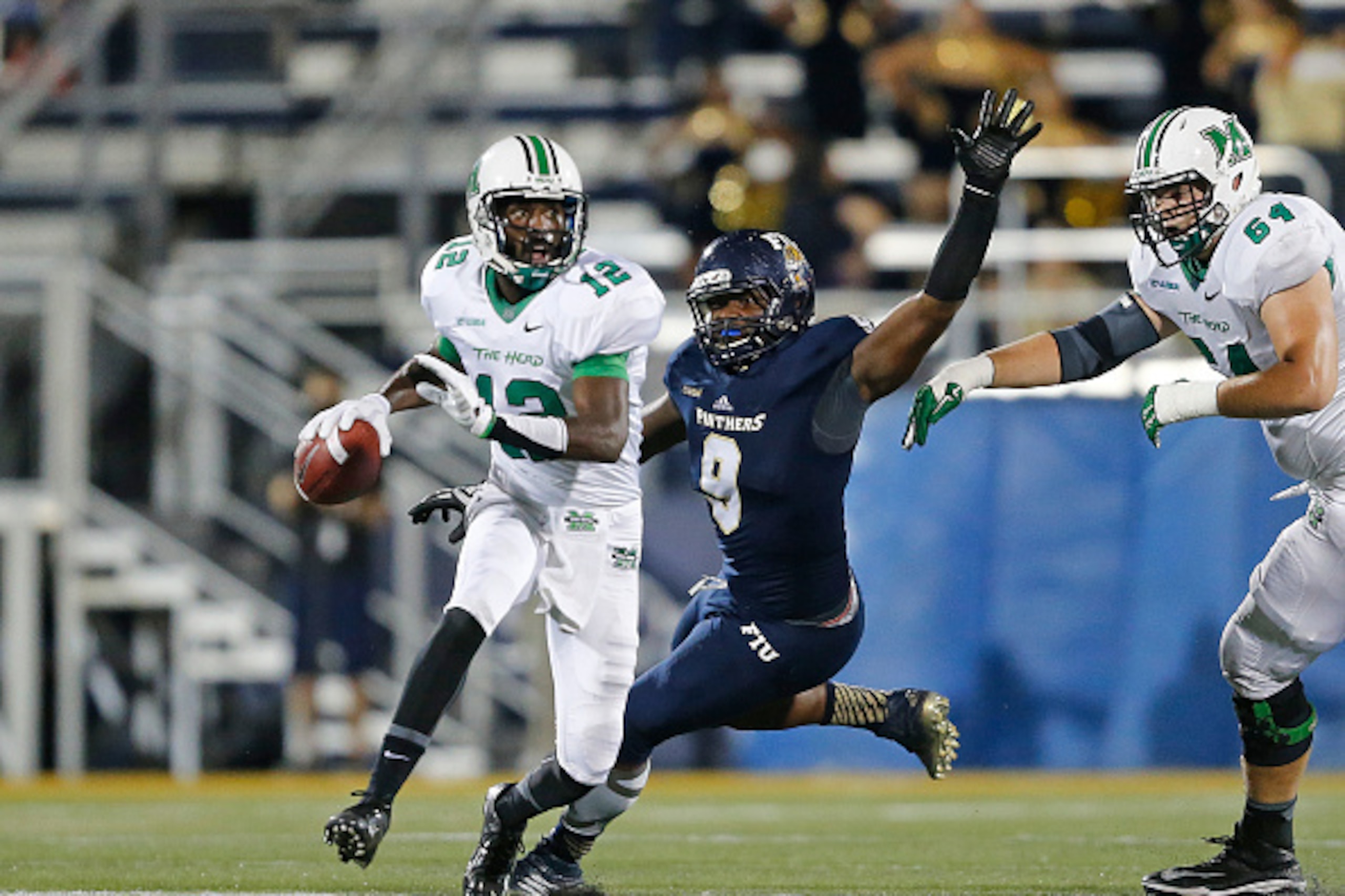 MIAMI, FL - OCTOBER 18: Rakeem Cato #12 of the Marshall Thundering Herd is pursued by Giovani Francois #9 of the Florida International Panthers as he scrambles out of the pocket with the ball on October 18, 2014 at FIU Stadium in Miami, Florida.Marshall d