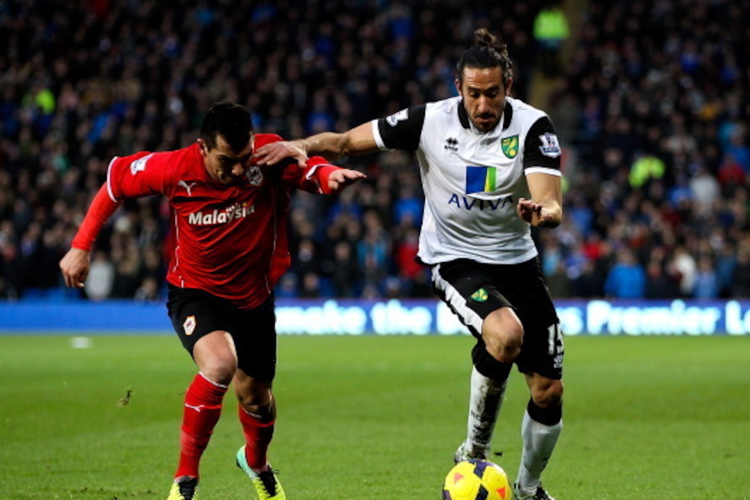 CARDIFF, WALES - FEBRUARY 01:  Jonas Gutierrez of Norwich holds off the challenge of Guy Medel of Cardiff during the Barclays Premier League match between Cardiff City and Norwich City at Cardiff City Stadium on February 1, 2014 in Cardiff, Wales.  (Photo