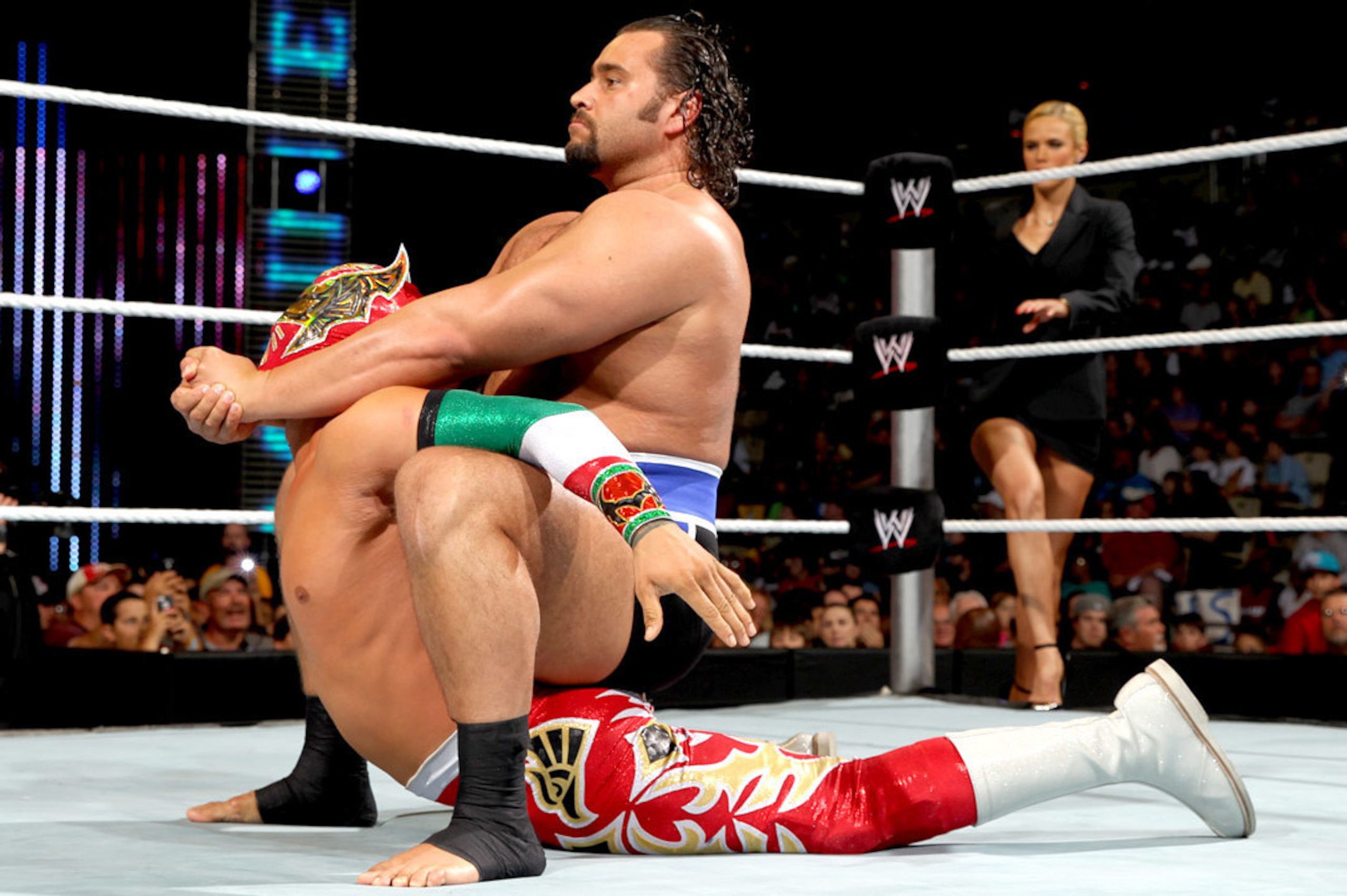 Rusev puts Sin Cara in the Camel Clutch.