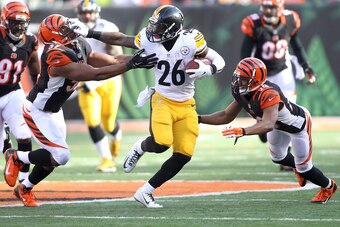 CINCINNATI, OH - DECEMBER 7:  Le'Veon Bell #26 of the Pittsburgh Steelers stiff arms Vincent Rey #57 of the Cincinnati Bengals as Leon Hall #29 of the Cincinnati Bengals dives in an attempt to make the tackle during the second quarter at Paul Brown Stadiu