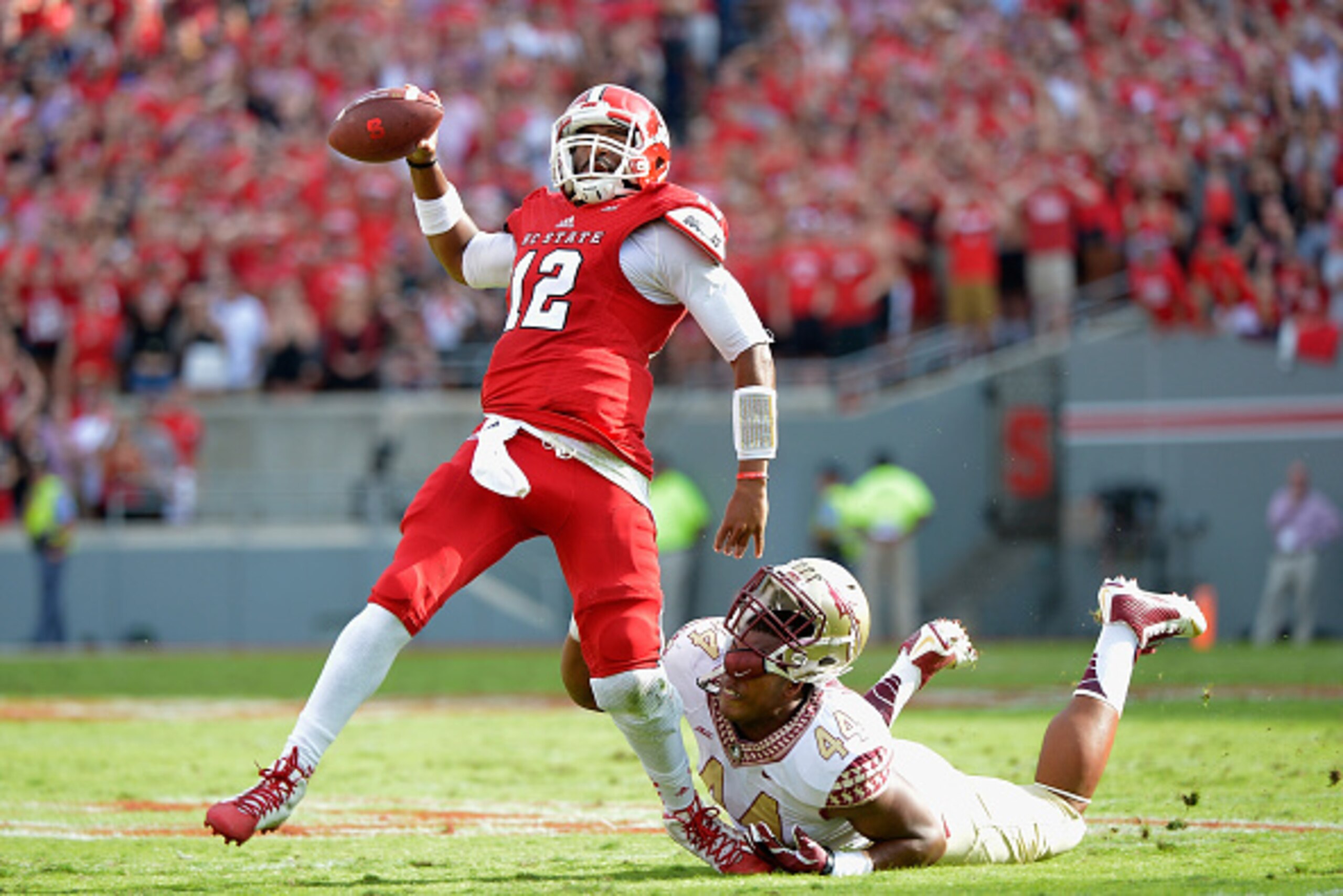 RALEIGH, NC - SEPTEMBER 27: Jacoby Brissett #12 of the North Carolina State Wolfpack breaks free from DeMarcus Walker #44 of the Florida State Seminoles to throw a touchdown pass during the first quarter of their game at Carter-Finley Stadium on September