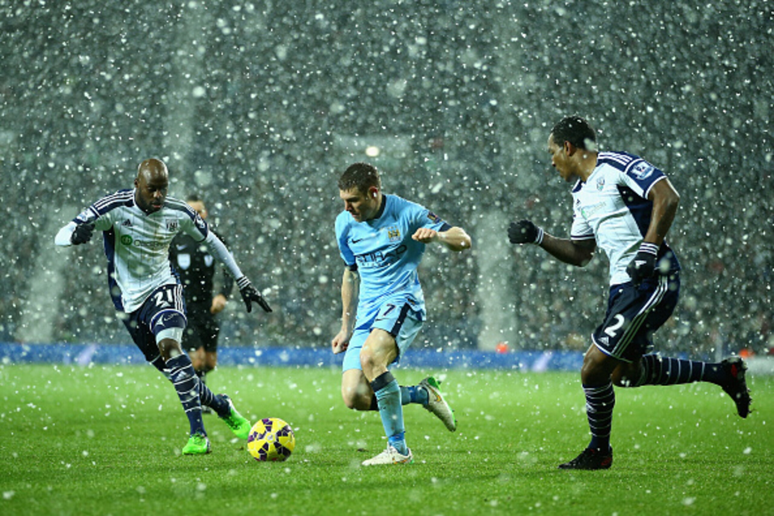 WEST BROMWICH, ENGLAND - DECEMBER 26:  James Milner of Manchester City takes on Youssuf Mulumbu and Andre Wisdom of West Brom as the snow falls during the Barclays Premier League match between West Bromwich Albion and Manchester City at The Hawthorns on D