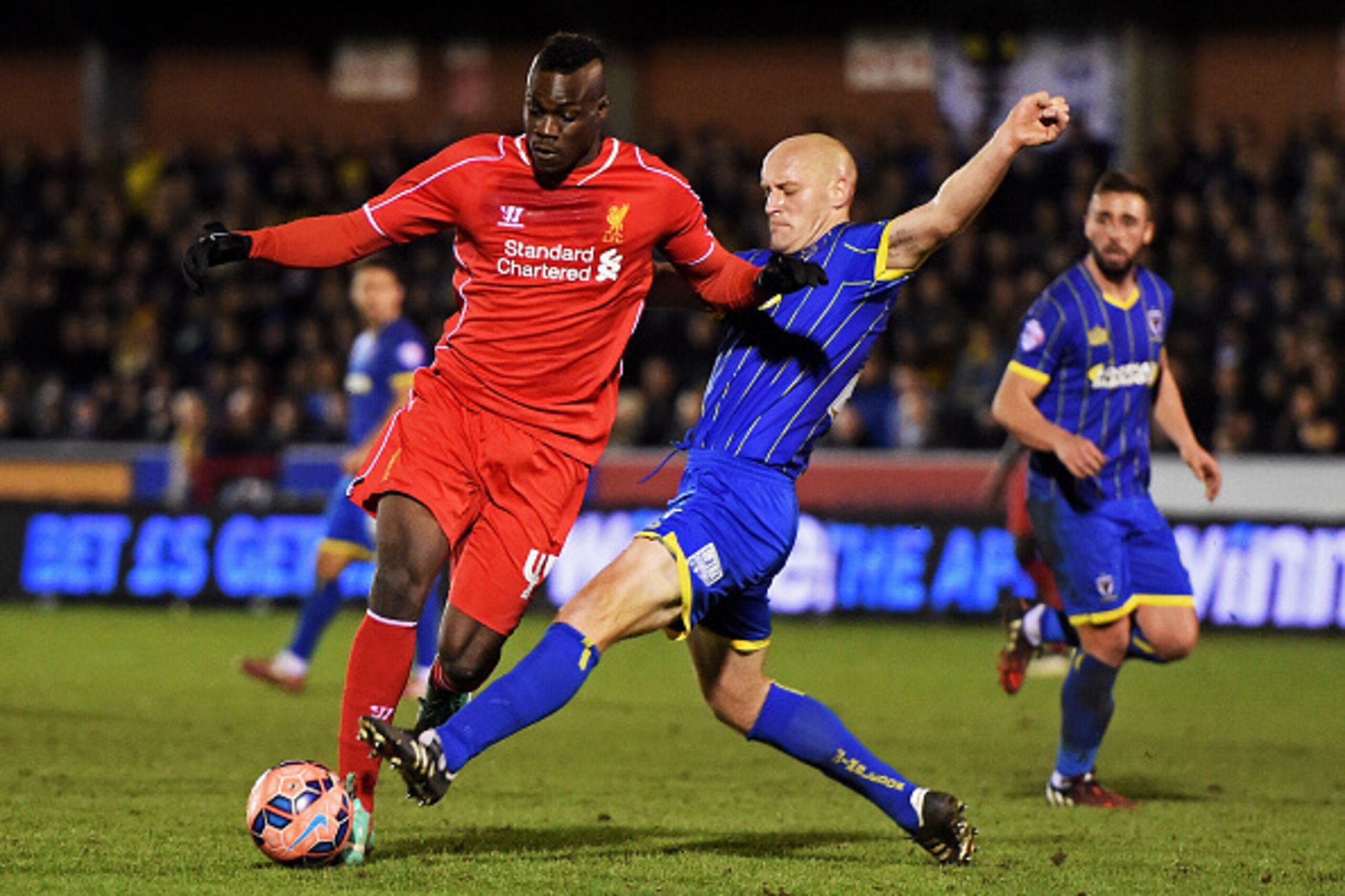 KINGSTON UPON THAMES, ENGLAND - JANUARY 05:  Mario Balotelli of Liverpool is tackled by Adam Barrett of AFC Wimbledon during the FA Cup Third Round match between AFC Wimbledon and Liverpool at The Cherry Red Records Stadium on January 5, 2015 in Kingston 