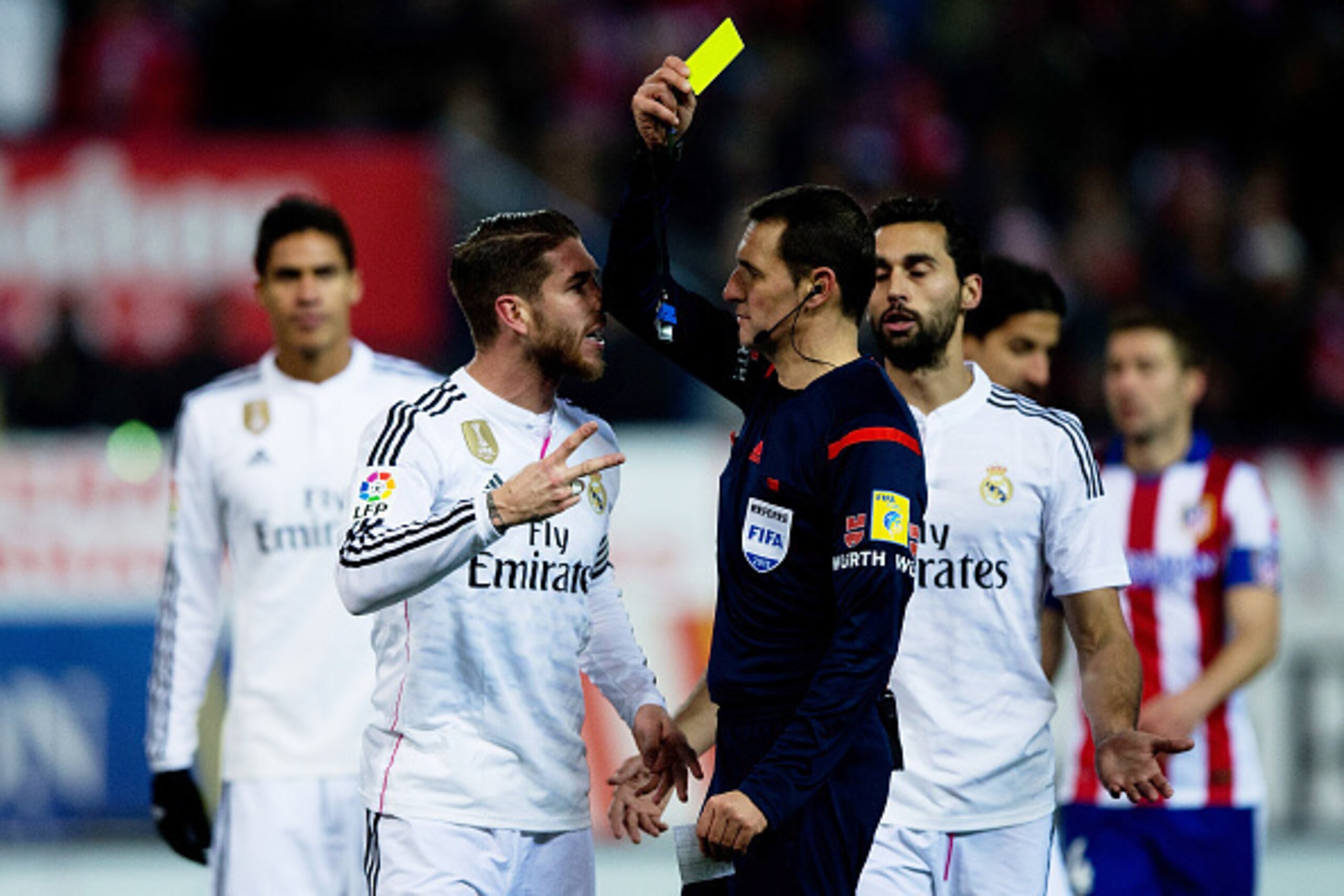 MADRID, SPAIN - JANUARY 07:  Sergio Ramos (L) of Real Madrid CF protests to the referee Close Gomez (R) as he shows the yellow card after a penalty over Raul Garcia of Atletico de Madrid during the Copa del Rey Round of 16  first leg match between Club At