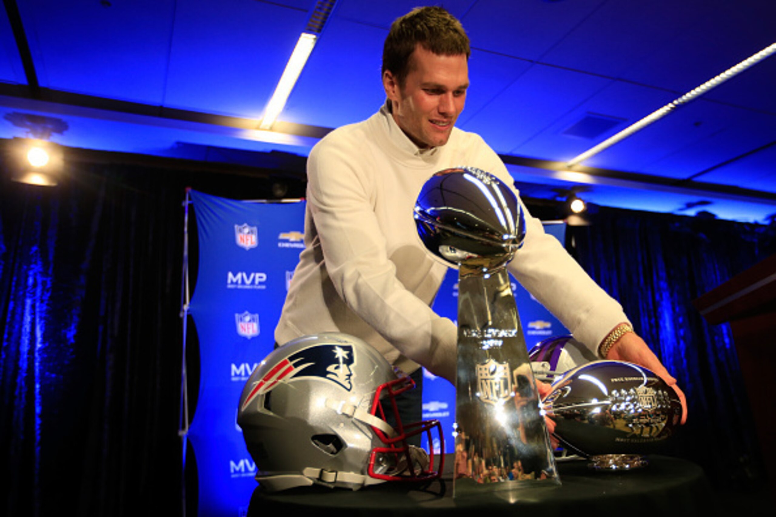 PHOENIX, AZ - FEBRUARY 02:  (L-R) Tom Brady of the New England Patriots picks up the Super Bowl XLIX MVP trophy during a Chevrolet Super Bowl XLIX MVP press conference folowing the Patriots Super Bowl win over the Seattle Seahawks on February 2, 2015 in P