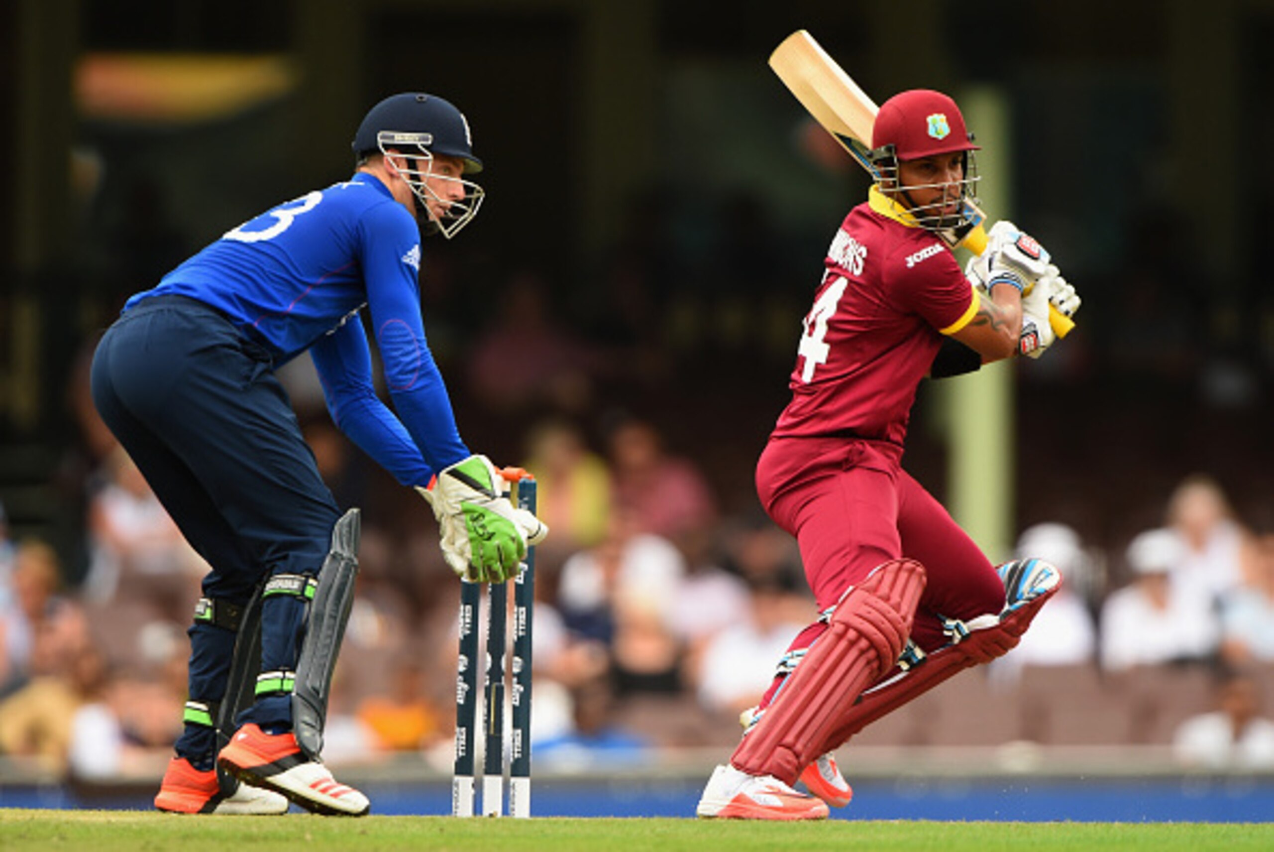 SYDNEY, AUSTRALIA - FEBRUARY 09:  Lendl Simmons of West Indies plays a shot as Jos Butler of England looks on during the ICC Cricket World Cup warm up match between England and the West Indies at Sydney Cricket Ground on February 9, 2015 in Sydney, Austra