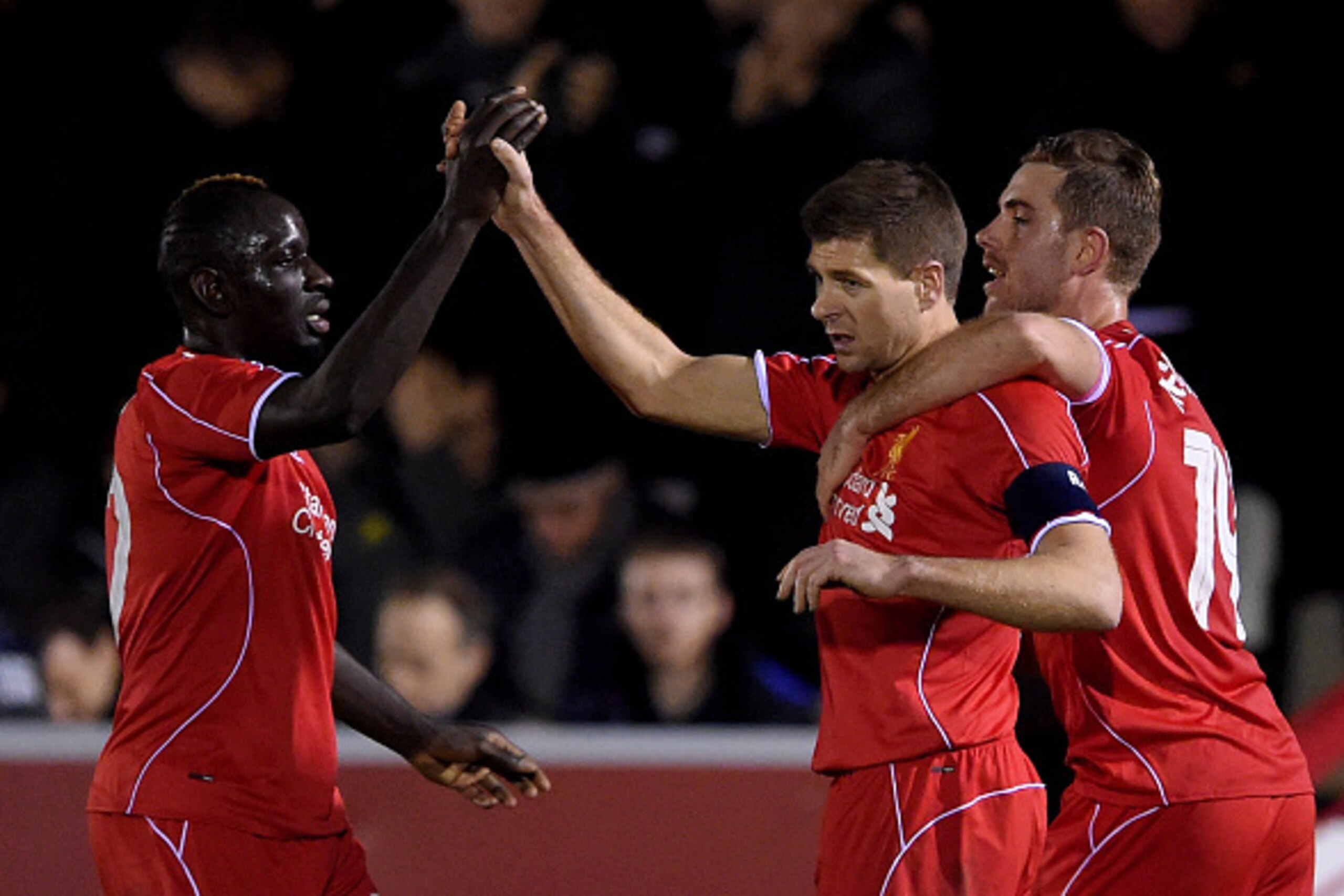 KINGSTON UPON THAMES, ENGLAND - JANUARY 05:  Steven Gerrard of Liverpool is congratulated by teammates Mamadou Sakho (L) and Jordan Henderson (R) after scoring his team's second goal from a free kick during the FA Cup Third Round match between AFC Wimbled