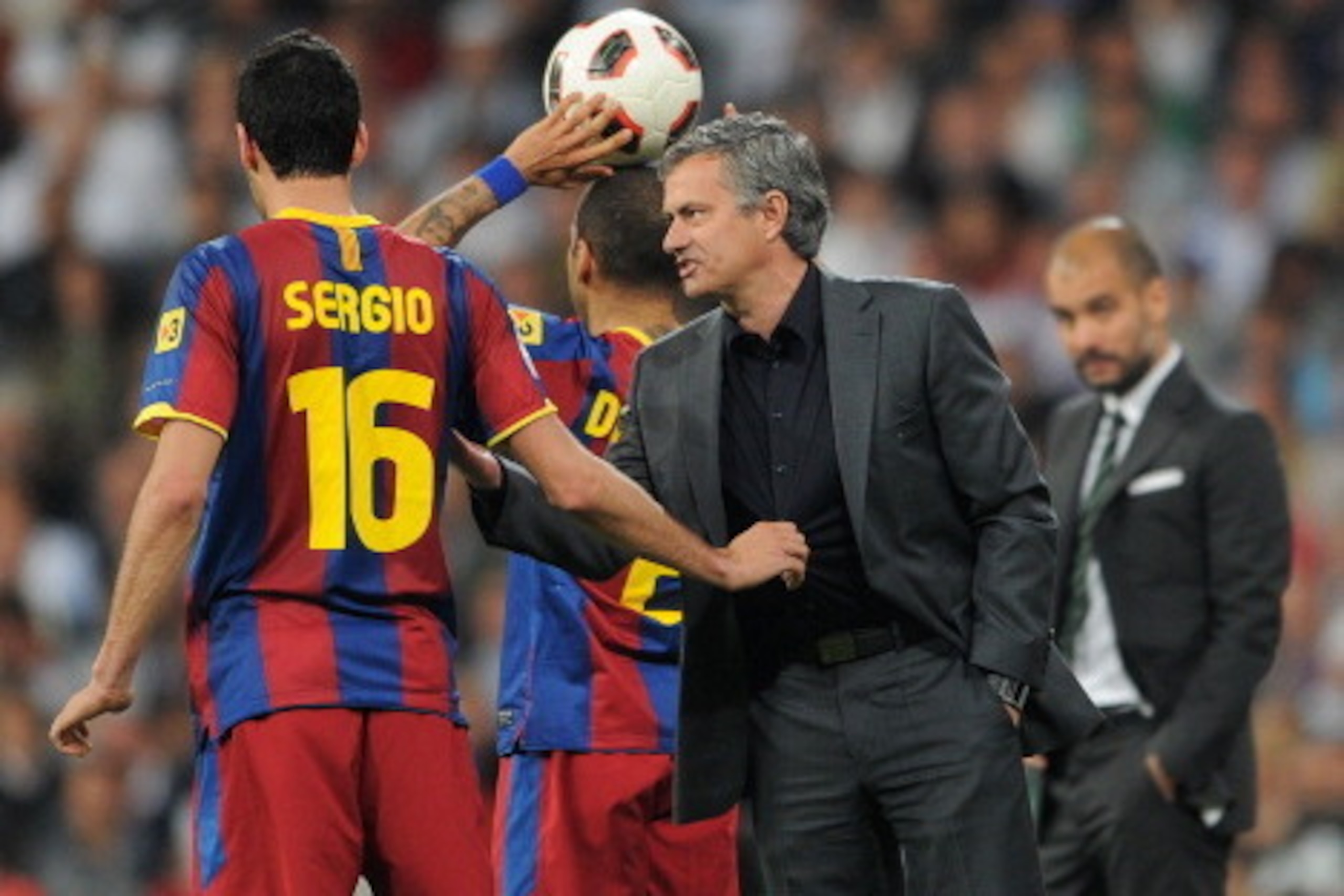 MADRID, SPAIN - APRIL 16:  Sergio Busquets (L) of Barcelona holds head coach Jose Mourinho (R) of Real Madrid by his shirt as they chat while head coach Josep Guardiola of Barcelona looks on in the background during the la Liga match between Real Madrid a