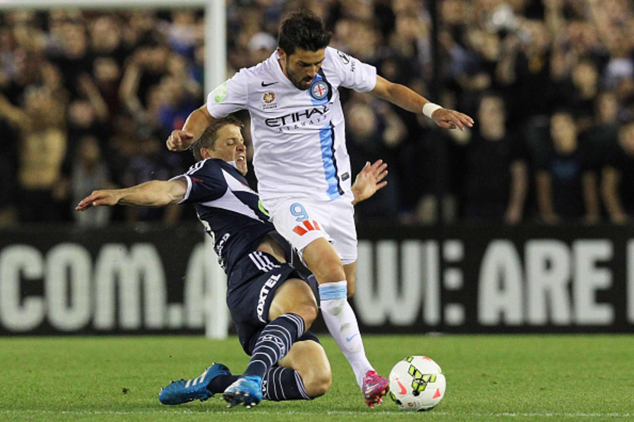 MELBOURNE, AUSTRALIA - OCTOBER 25:  David Villa (#9) of Melbourne City is tackled by Adrian Leijer (#23) of Melbourne Victory during the round three A-League match between the Melbourne Victory and Melbourne City at Etihad Stadium on October 25, 2014 in M
