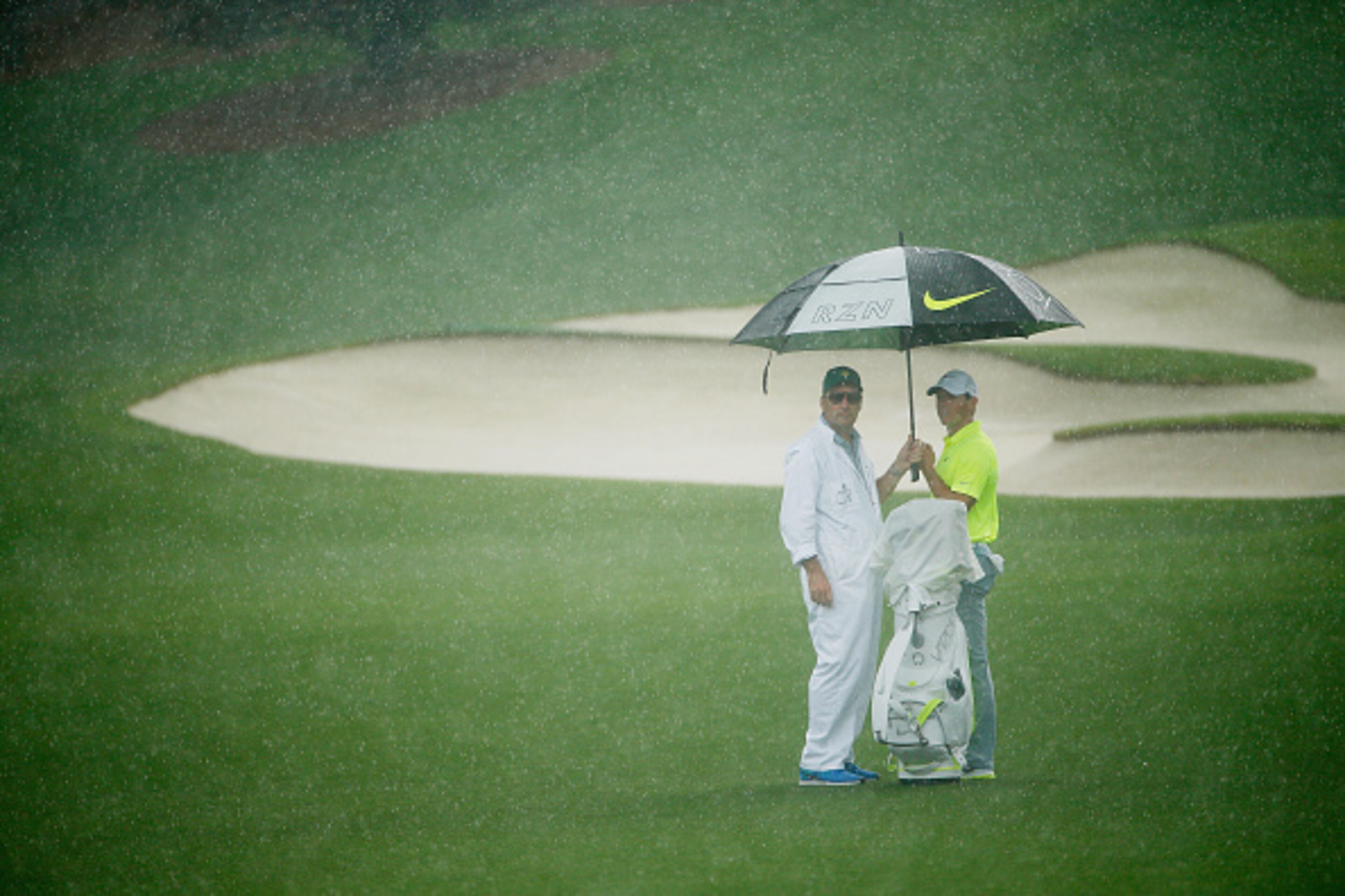 AUGUSTA, GA - APRIL 07:  Rory McIlroy of Northern Ireland waits with his caddie J.P. Fitzgerald in the rain during a practice round prior to the start of the 2015 Masters Tournament at Augusta National Golf Club on April 7, 2015 in Augusta, Georgia.  (Pho