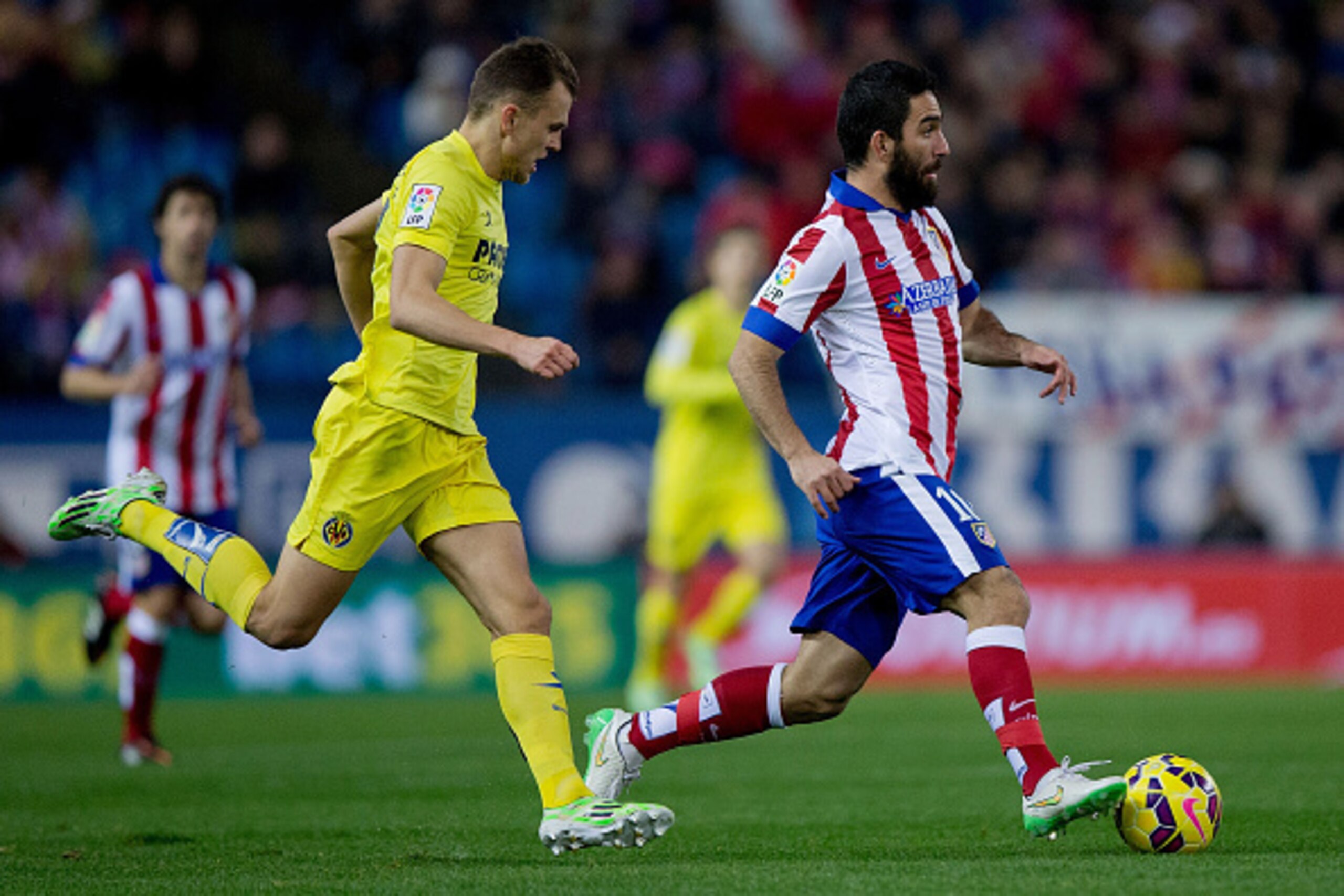 MADRID, SPAIN - DECEMBER 14: Arda Turan (R) of Atletico de Madrid runs with the ball ahead of Denis Cheryshev (L) of Villarreal CF during the La Liga match between Club Atletico de Madrid and Villarreal CF at Vicente Calderon Stadium on December 14, 2014 