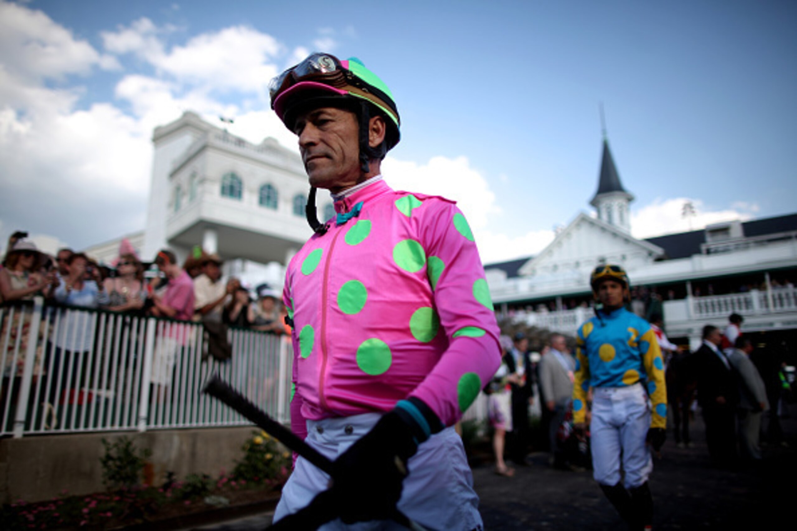 LOUISVILLE, KY - MAY 02:  Jockey Gary Stevens of Firing Line #10 walks ahead of Jockey Victor Espinoza of American Pharoah #18 in the paddock area prior to the 141st running of the Kentucky Derby at Churchill Downs on May 2, 2015 in Louisville, Kentucky. 