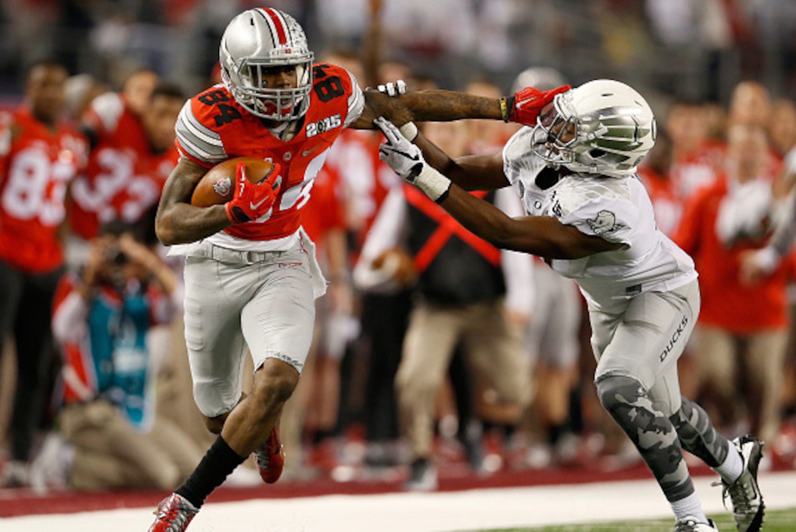 ARLINGTON, TX - JANUARY 12:  Wide receiver Corey Smith #84 of the Ohio State Buckeyes stiff arms Reggie Daniels of the Oregon Ducks before fumbling the ball in the second quarter during the College Football Playoff National Championship Game at AT&T Stadi