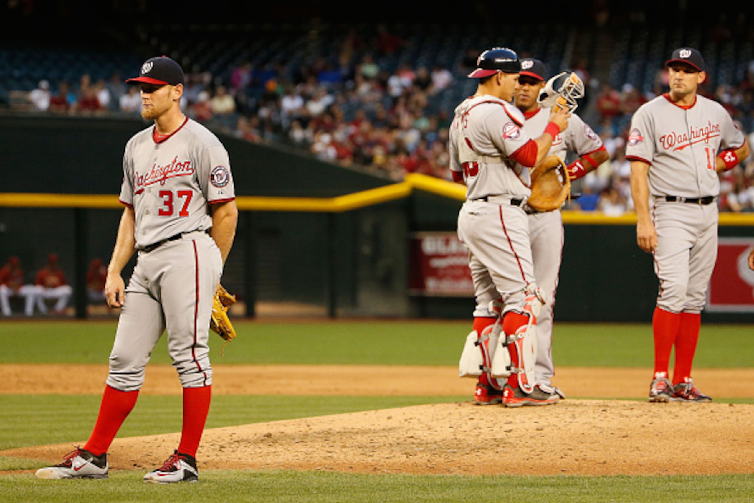 PHOENIX, AZ - MAY 12:  Starting pitcher Stephen Strasburg #37 of the Washington Nationals stands on the field with teammates as team trainers attend to home-plate umpire Kerwin Danley (not pictured) during the second inning of the MLB game at Chase Field