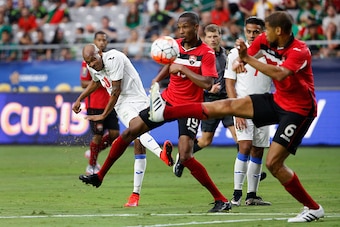 GLENDALE, AZ - JULY 12:  Ariel Martinez #10 of Cuba shoots the ball past Kevan George #19 and Radanfah Abu Bakr #6 of Trinidad & Tobago during the second half of the 2015 CONCACAF Gold Cup group C match at University of Phoenix Stadium on July 12, 2015 in
