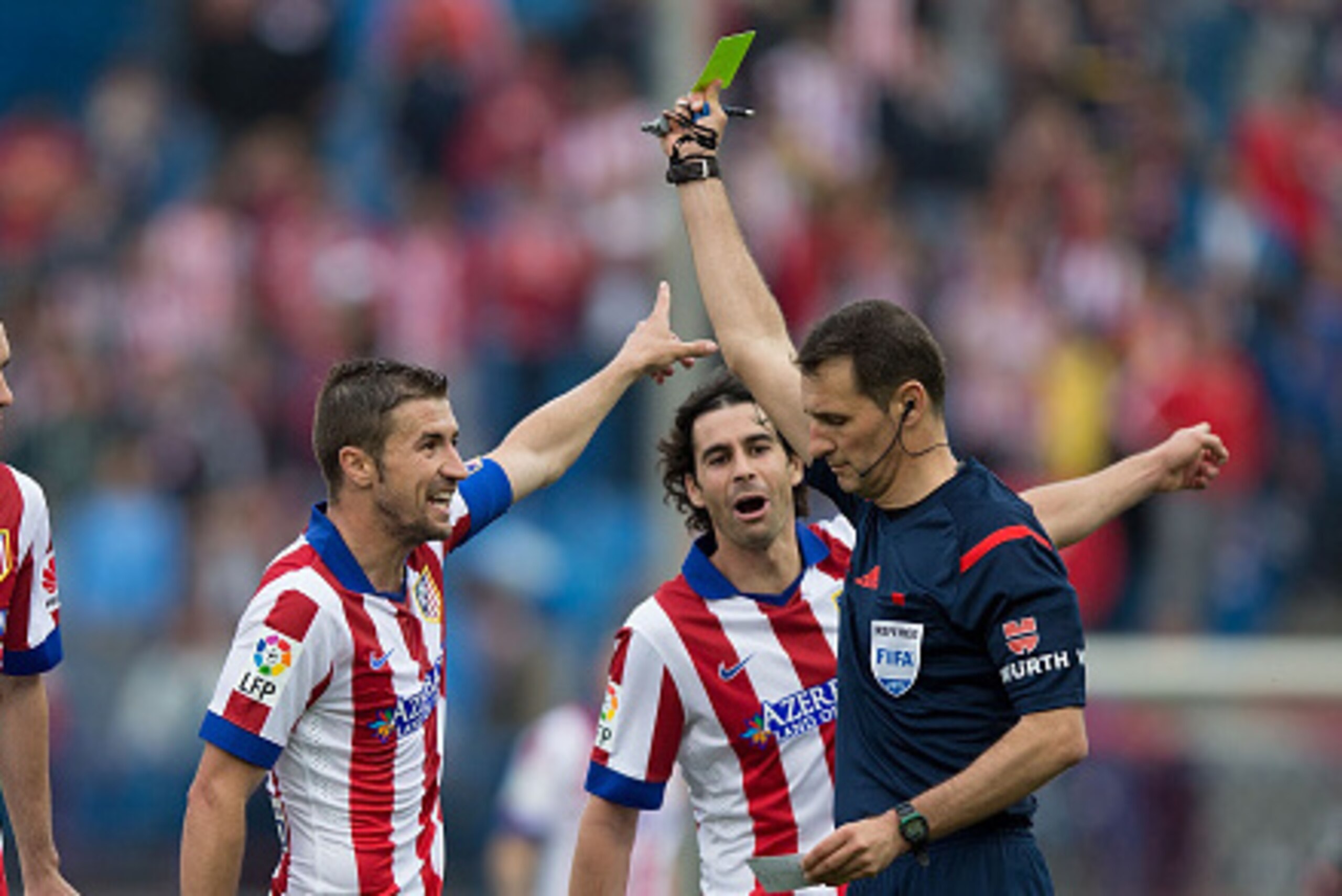 MADRID, SPAIN - APRIL 25: referee Clos Gomez (R) shiws the yellow card to Gabi Fernandez (2ndL) as his teammates Diego Godin (L) and Tiago Mendes (2ndR) protest during the La Liga match between Club Atletico de Madrid and Elche FC at Vicente Calderon Stad