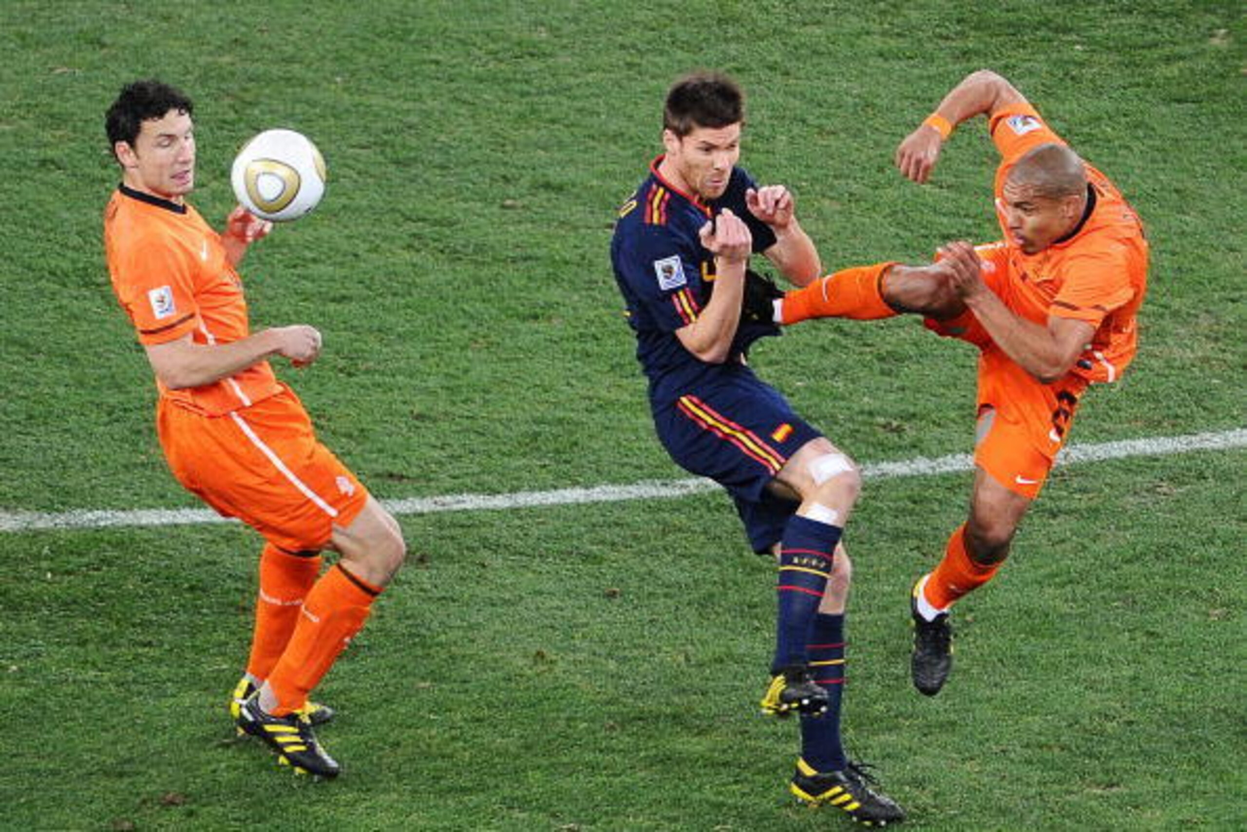 Netherlands' midfielder Nigel de Jong (R) fouls Spain's midfielder Xabi Alonso (C) with a kick to the stomach as Netherlands' midfielder Mark van Bommel (L) looks on during the 2010 World Cup football final between the Netherlands and Spain on July 11, 20