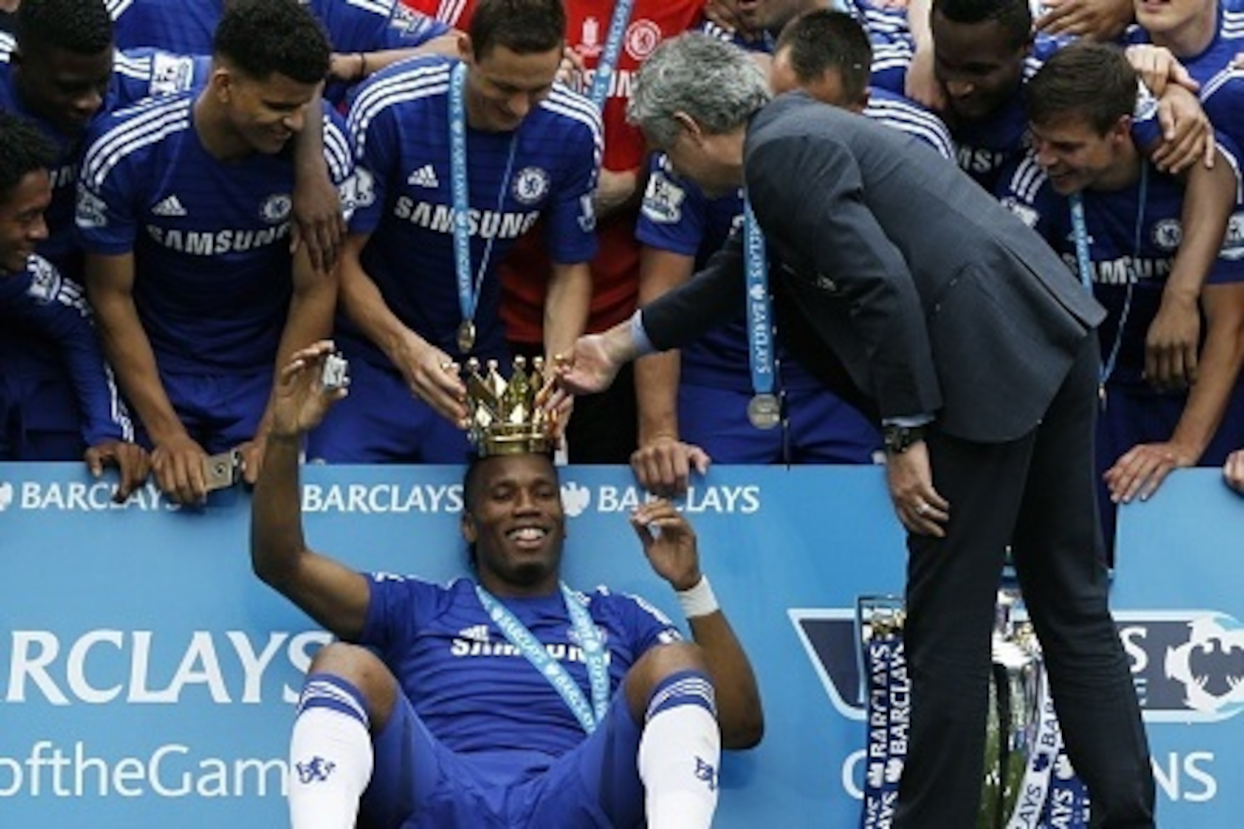 Chelsea's Serbian midfielder Nemanja Matic (top C) and Chelsea's Portuguese manager Jose Mourinho (R) place the crown of the Premier League trophy on the head of Chelsea's Ivorian striker Didier Drogba (bottom C) surrounded by team-mates during the trophy