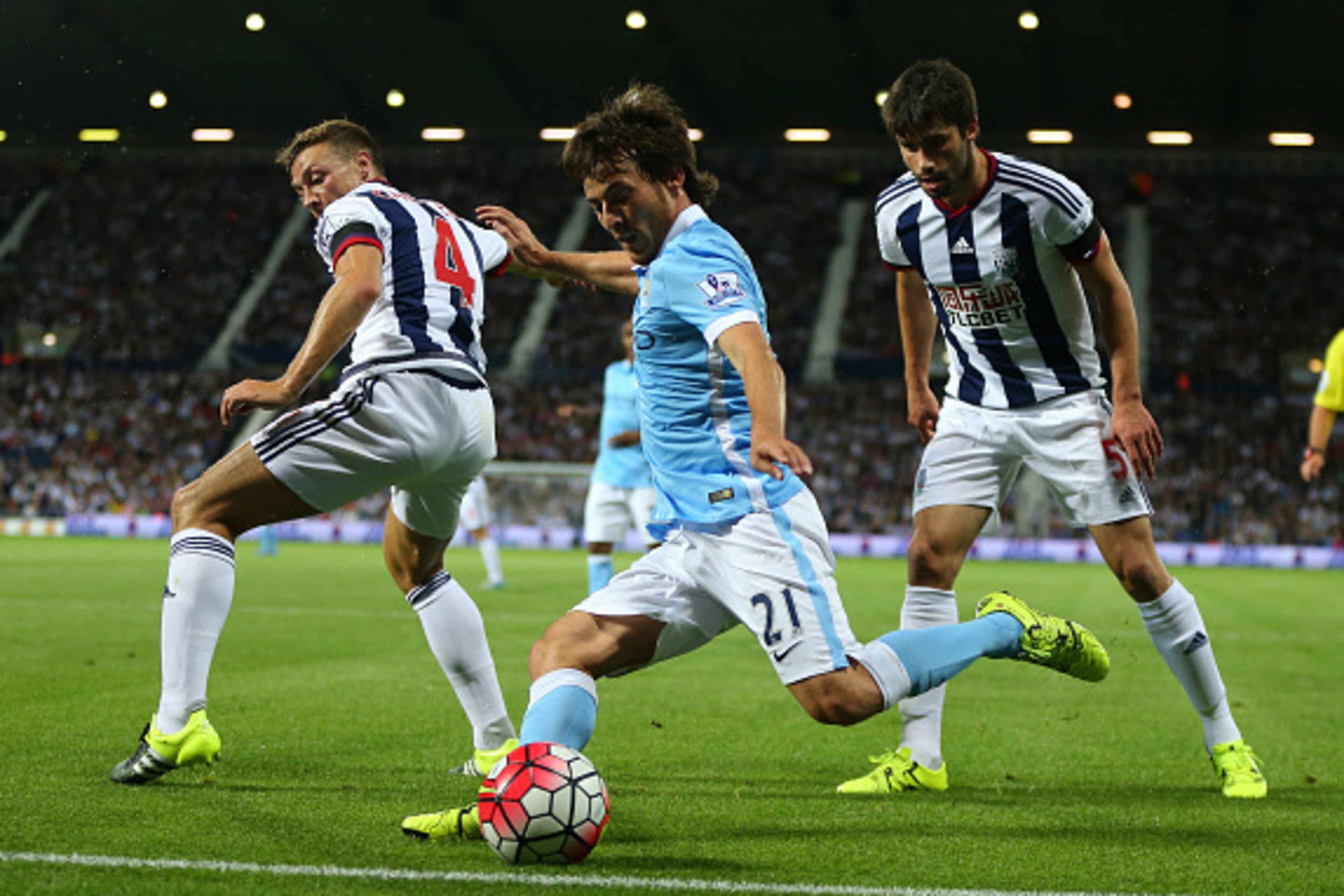 WEST BROMWICH, ENGLAND - AUGUST 10: David Silva of Manchester City crosses the ball past James Chester and Claudio Yacob of West Bromwich Albion, from which Vincent Kompany of Manchester City scores to make it 0-3 during the Barclays Premier League match 