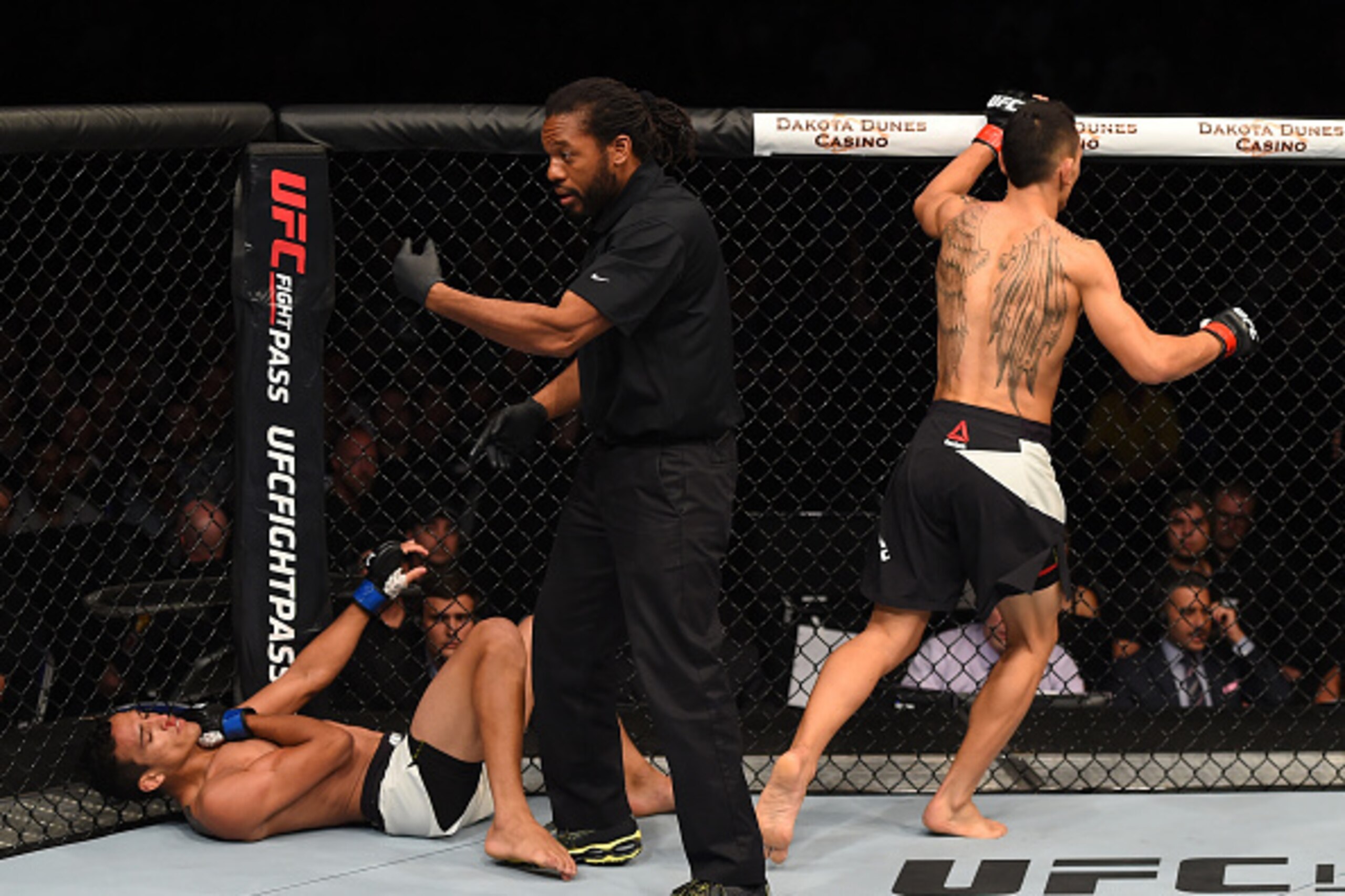 SASKATOON, SK - AUGUST 23:  Referee Herb Dean (C) calls for the doctor as Charles Oliveira (L) of Brazil falls to the ground with an injury against Max Holloway of the United States in their featherweight bout during the UFC event at the SaskTel Centre on