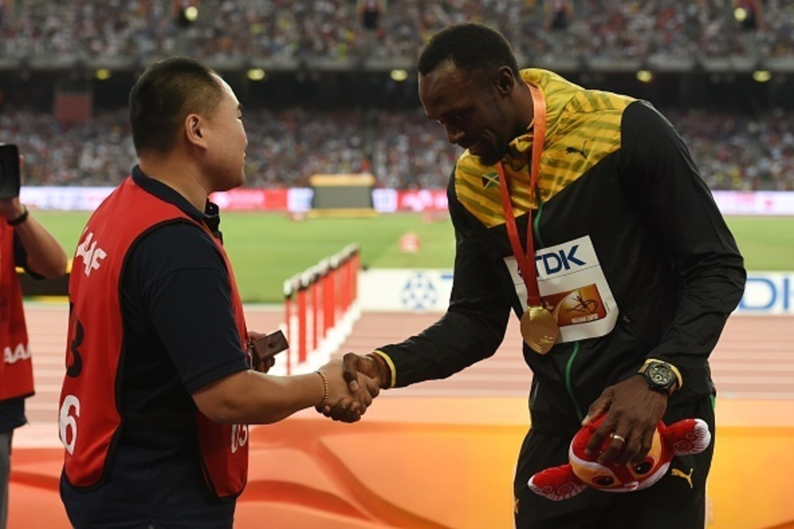 Chinese broadcast journalist Tao Song (L) shakes hands with Jamaica's gold medallist Usain Bolt (R) as he presents him a gift during the victory ceremony for the men's 200 metres athletics event at the 2015 IAAF World Championships at the 'Bird's Nest' Na